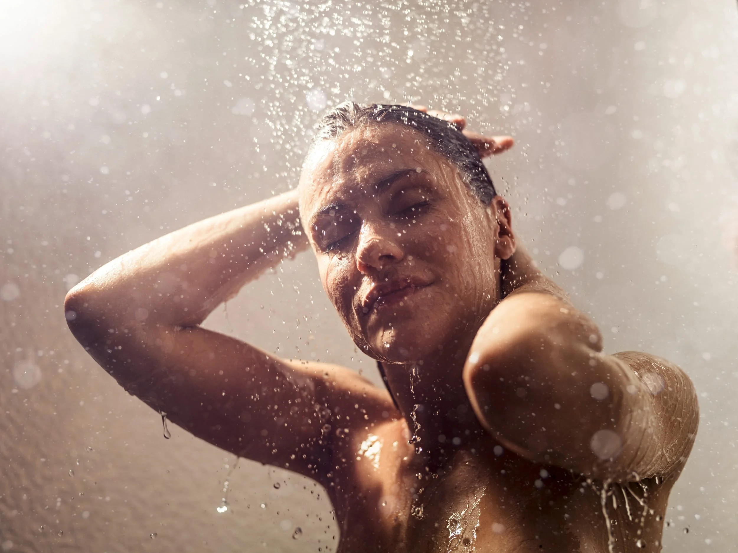 Frau unter der Dusche mit Wassertropfen im Gegenlicht