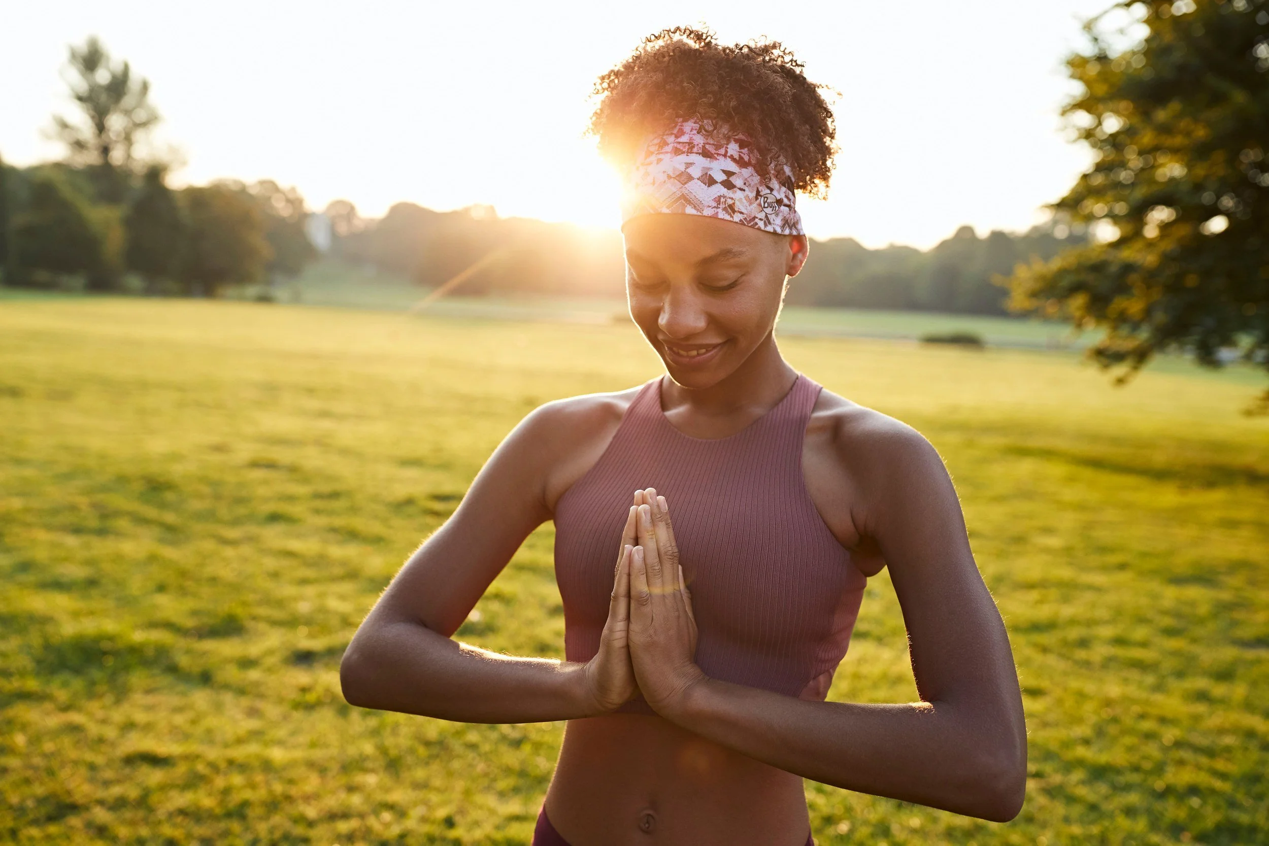 Yogini mit gemustertem BUFF Stirnband in Namaste-Pose bei Abendsonne