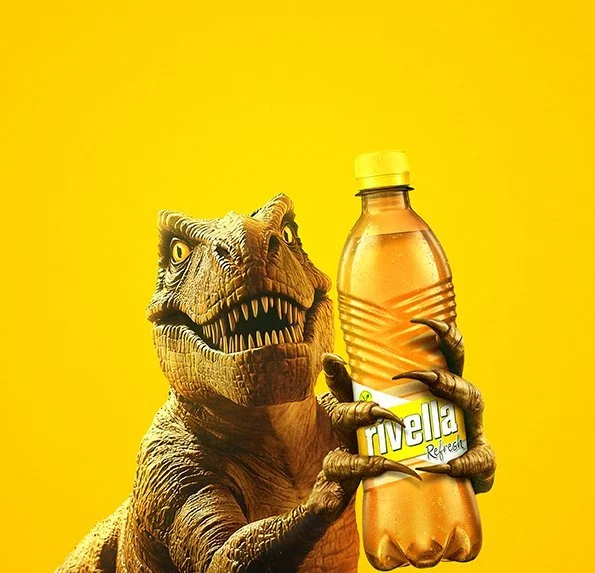 T-Rex hält Rivella-Flasche vor gelbem Grund, verspieltes Composing „Mach’s Farbig“ für Rivella – Bildergut.