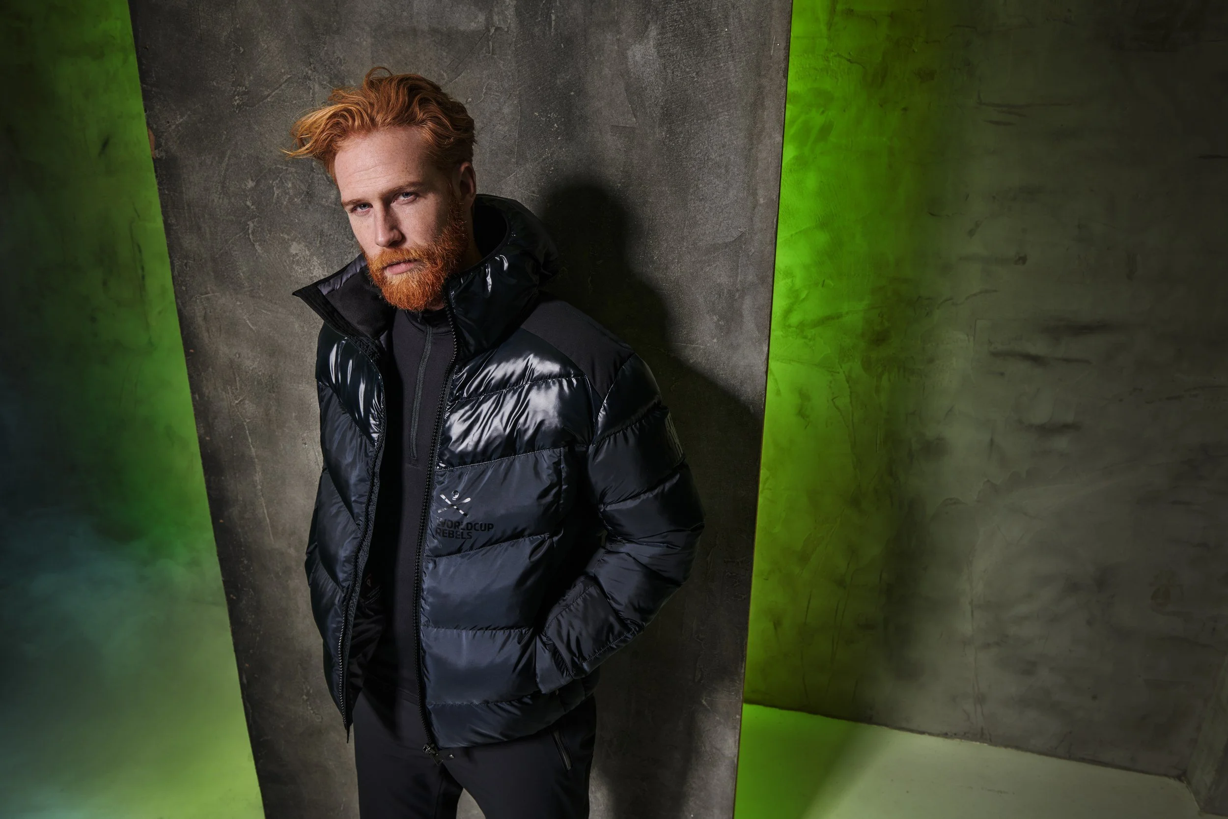 Mann in schwarzer Daunenjacke vor grün-grauem Set