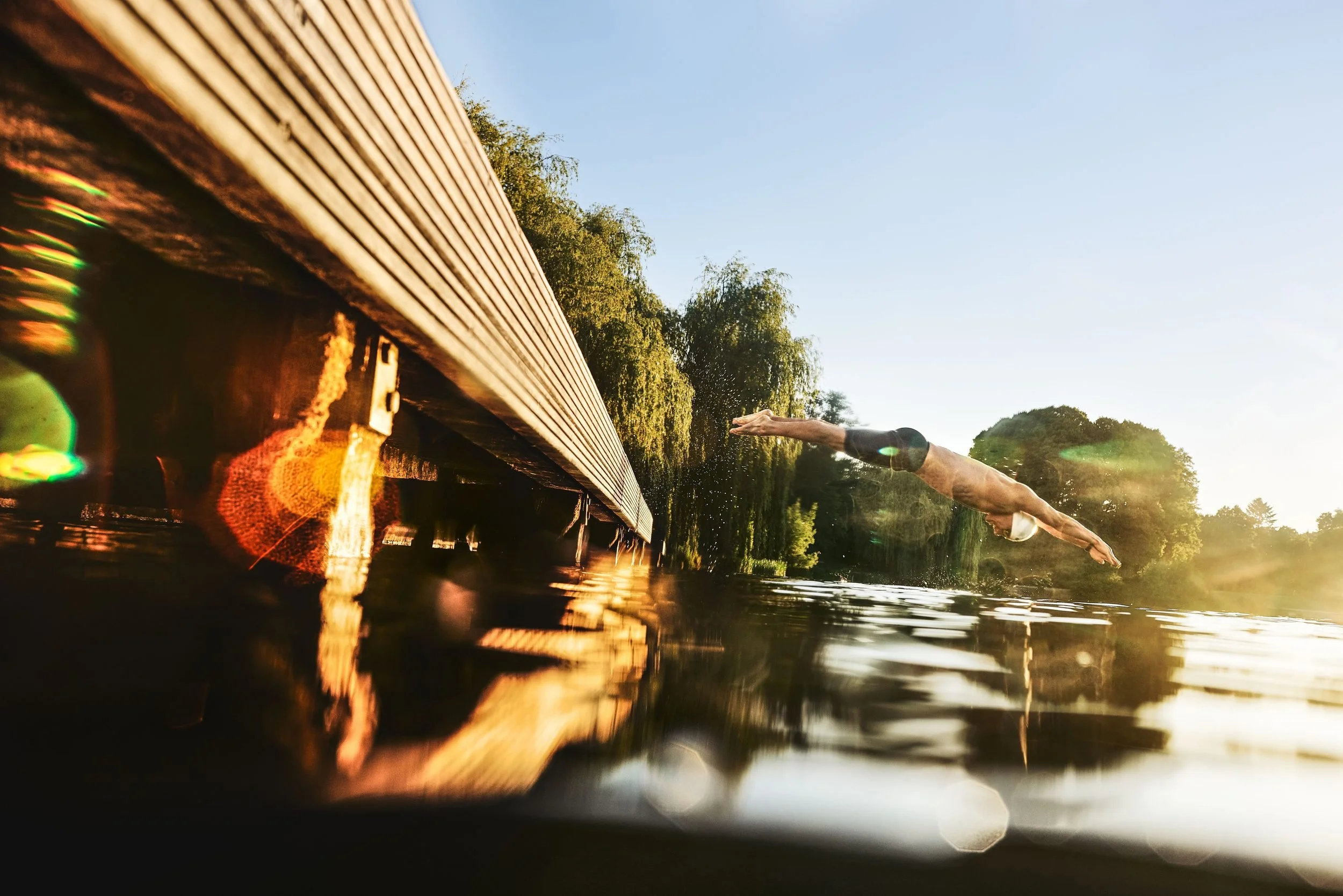 Schwimmer-Editorial von Tim Wendrich: Sprung vom Steg unter dem Holzdach im warmen Morgenlicht