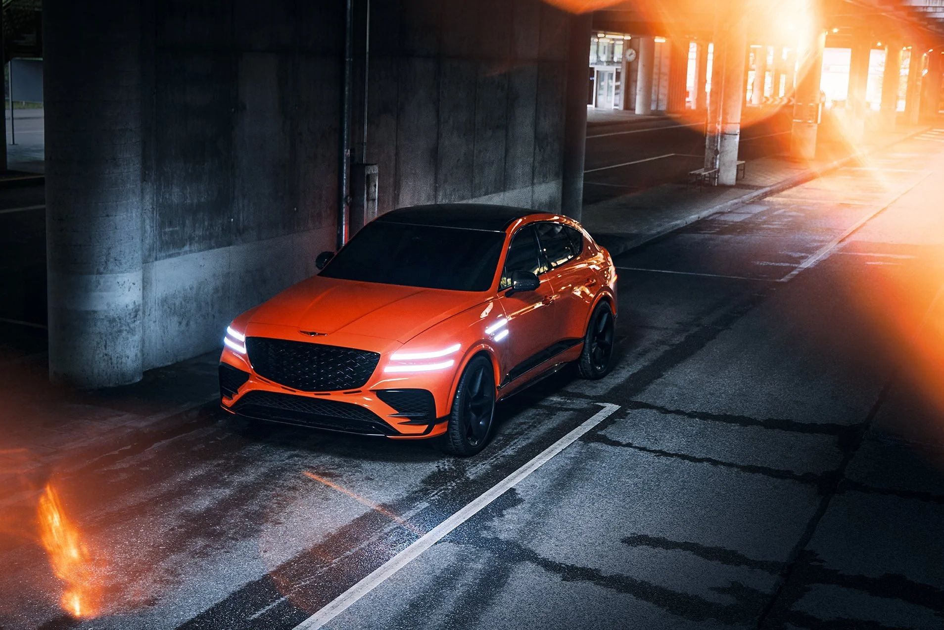 Orangefarbener Genesis GV80 SUV nachts unter Betonbrücke mit Lens-Flare – Retusche Bildergut.