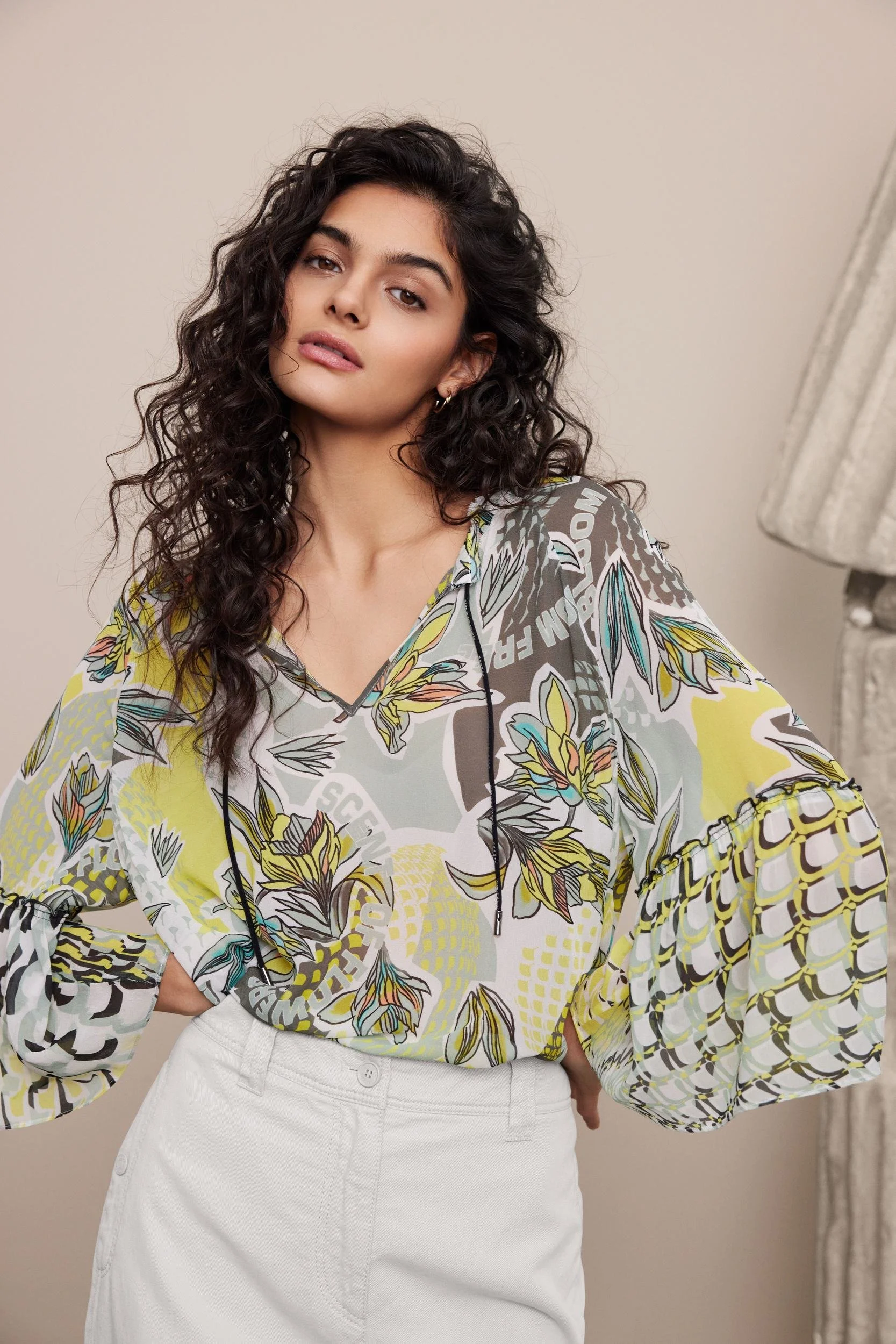 Modehaus Zinser Frühjahr-Sommer 2024: Bluse mit Blätterprint zu weißer Hose vor Säulenfragmenten