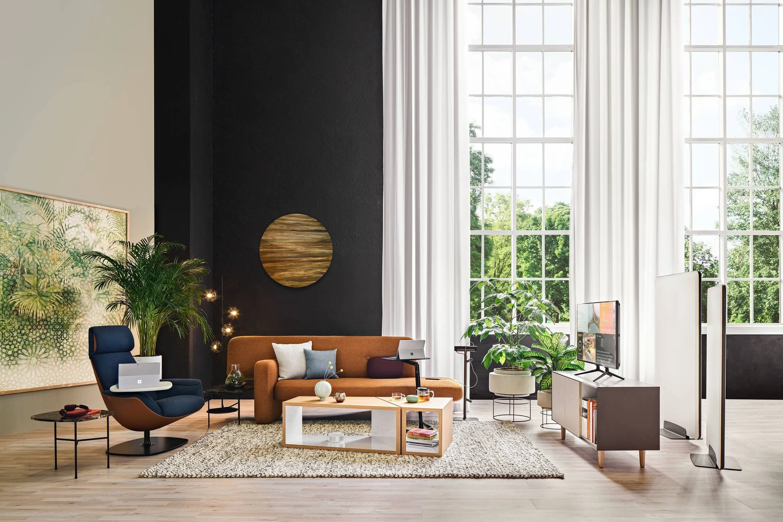 Elegante Lounge mit orangefarbenem Steelcase Sofa vor hohen Fenstern