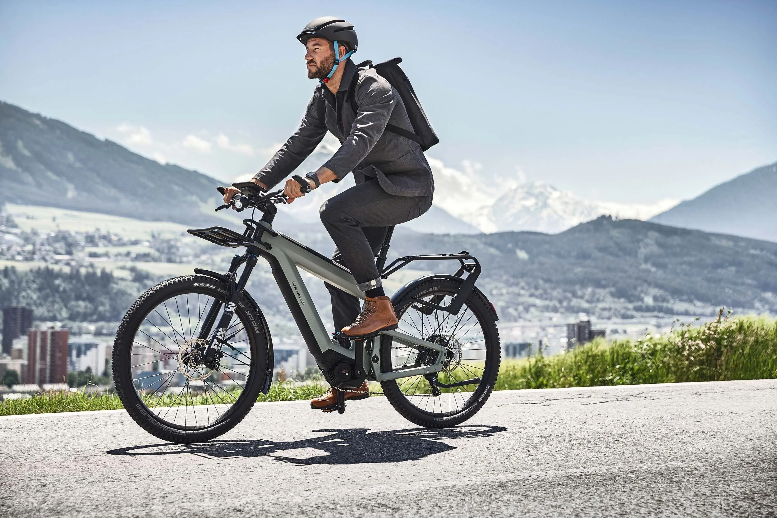 Mann pendelt mit E-Bike, Stadt und Berge im Hintergrund