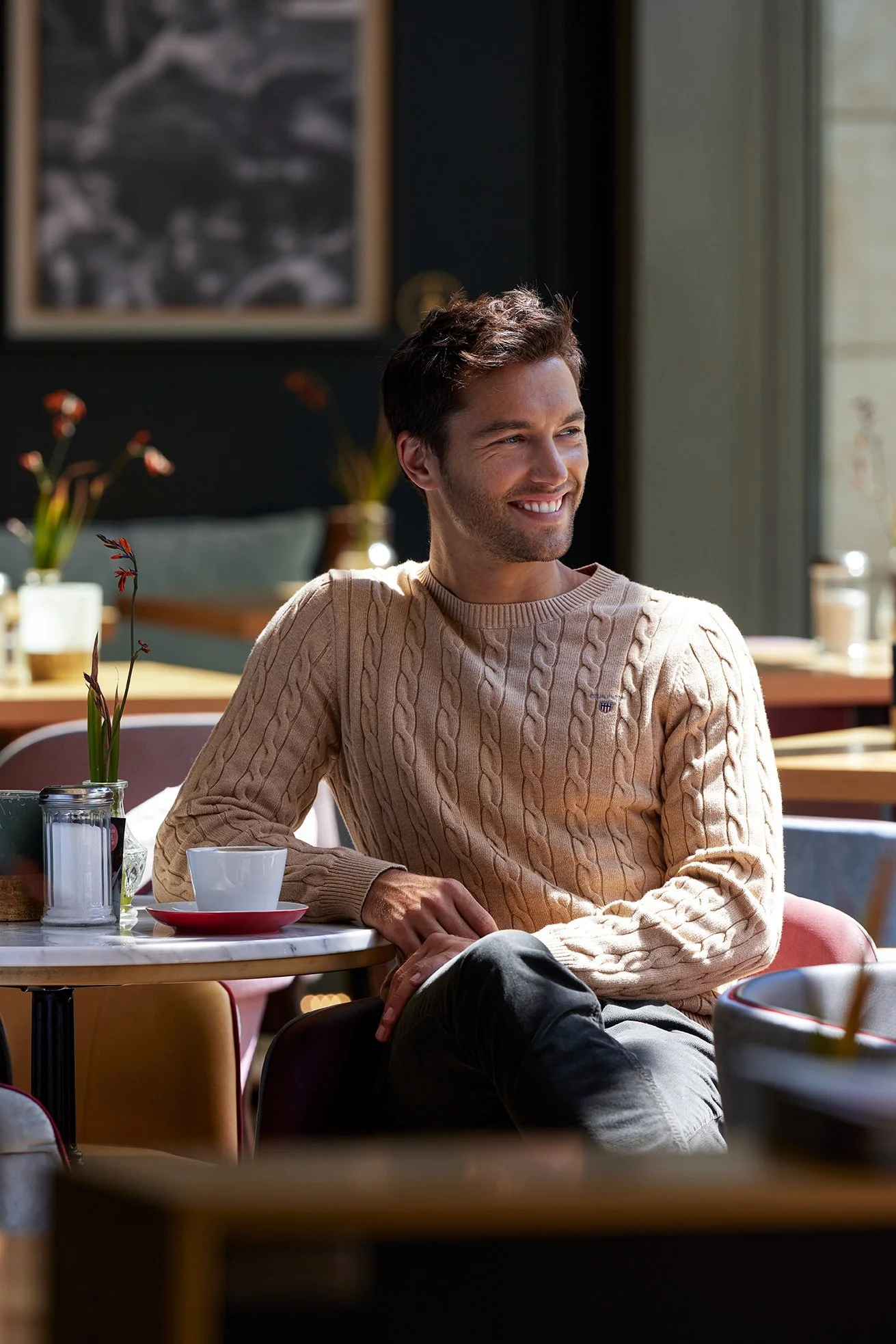 Mann im beigen Zopfstrickpullover im warm belichteten Café, Classic-Kampagne 2022 für Zinser – Retusche Bildergut.
