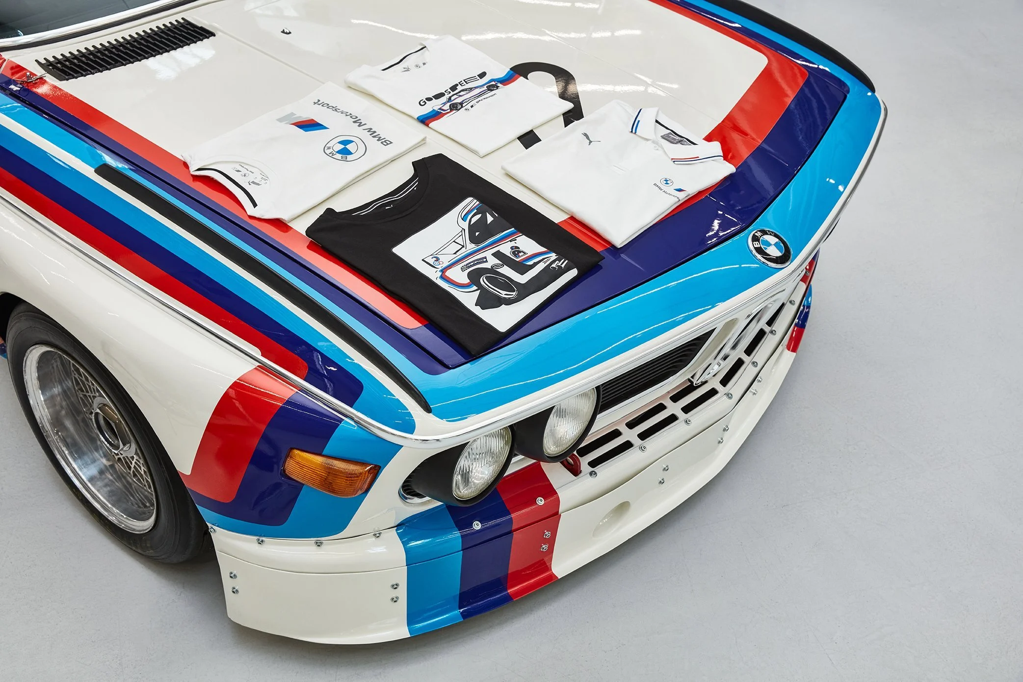 Klassischer BMW im M-Motorsport-Design mit Merchandise-Shirts auf der Motorhaube – Retusche Bildergut.