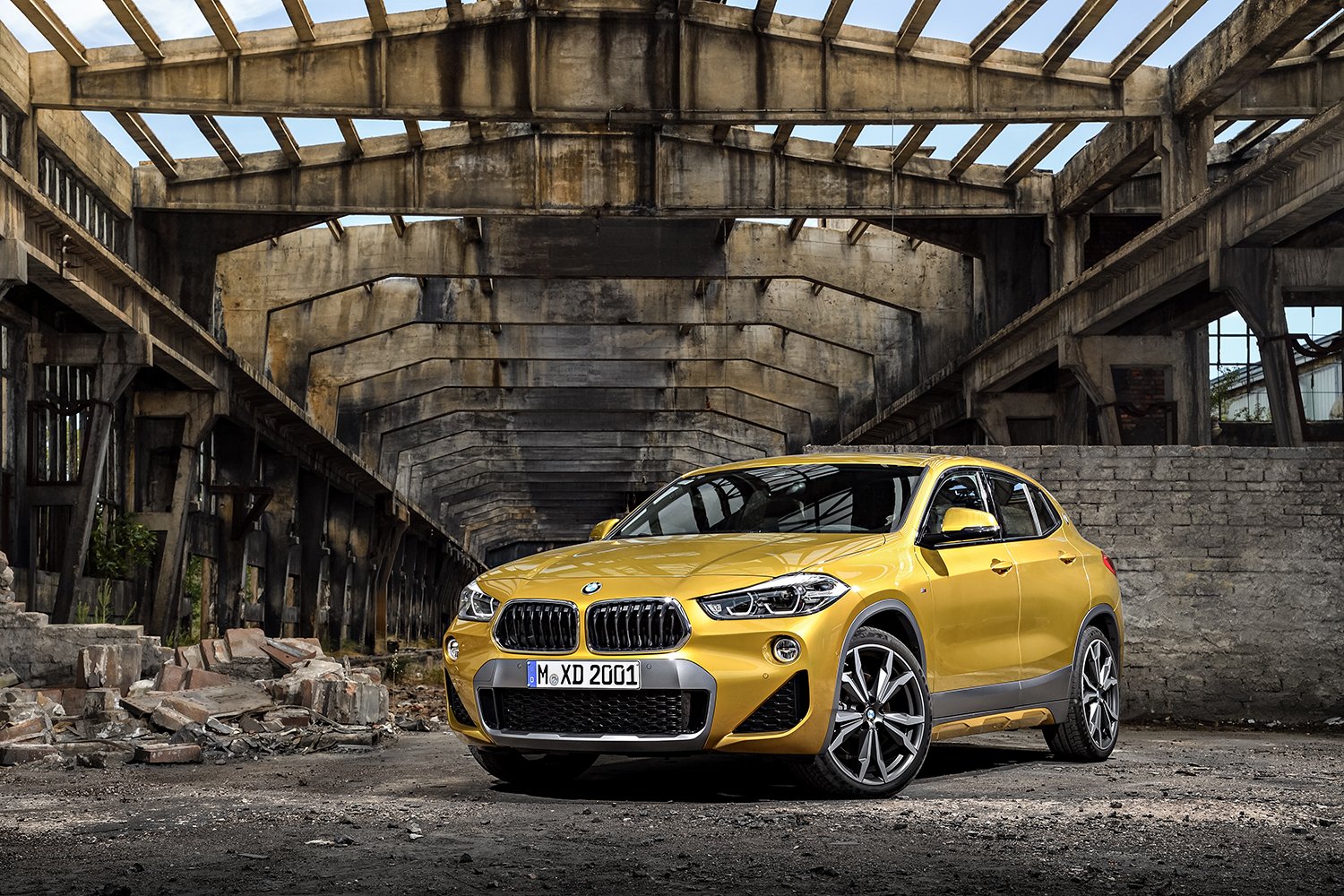 Goldgelber BMW X2 in einer verfallenen Industriehalle aus rohem Beton – High-End-Retusche von Bildergut.