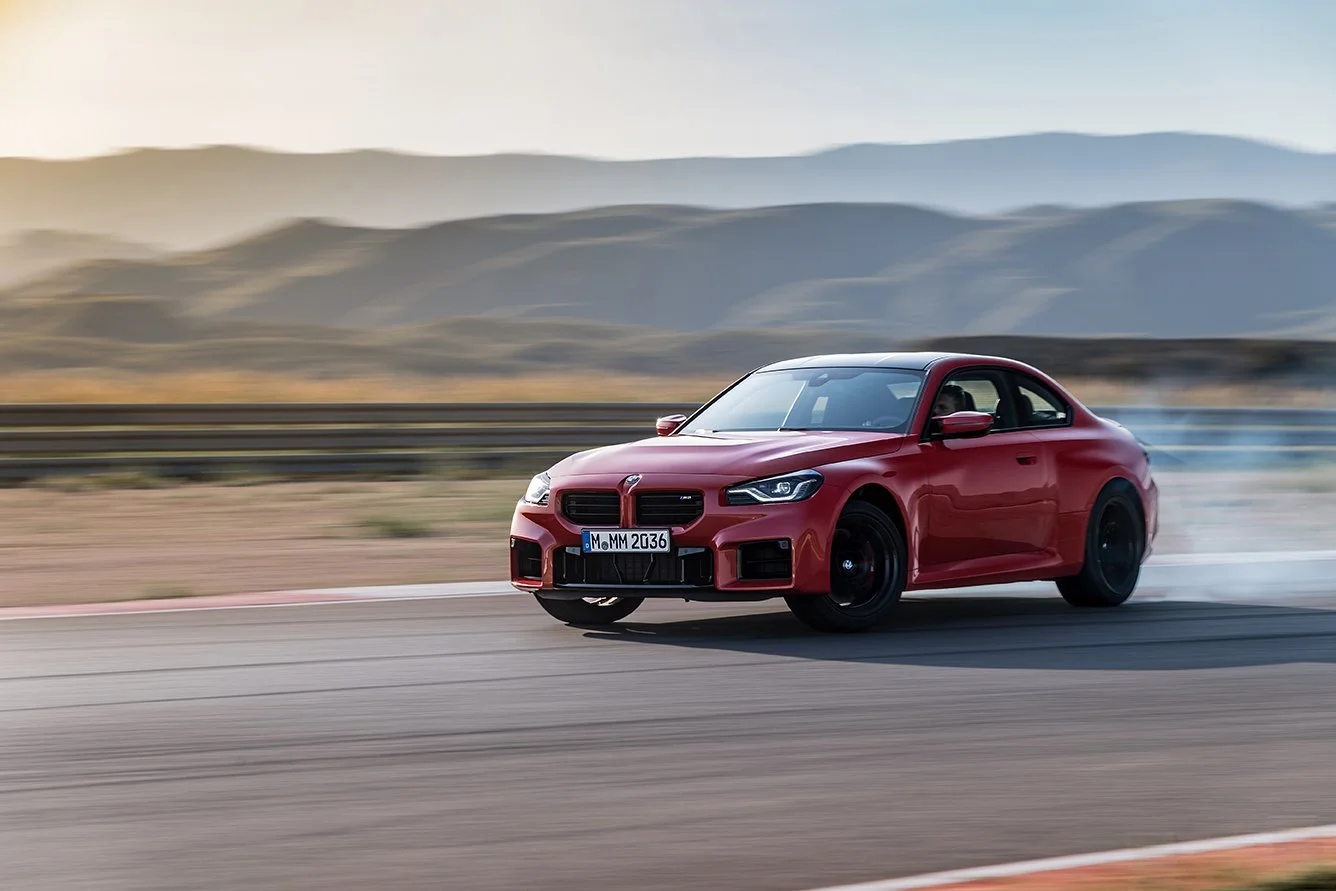 Roter BMW M2 driftet mit Reifenrauch auf der Rennstrecke vor Bergkulisse – High-End-Retusche von Bildergut.