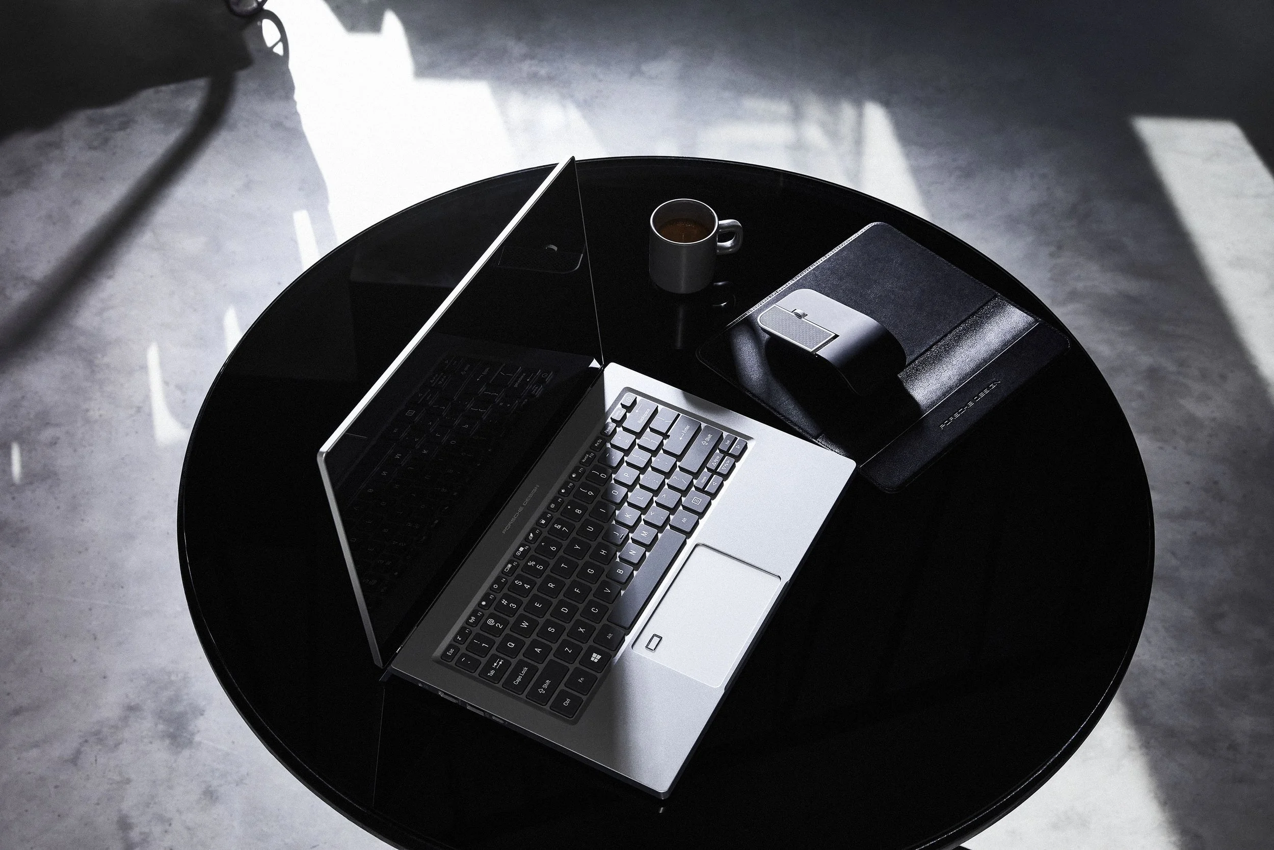 Silbernes Notebook mit Espresso und Maus auf schwarzem Tisch, Schwarz-Weiß-Kampagne für Porsche Design – Retusche Bildergut.