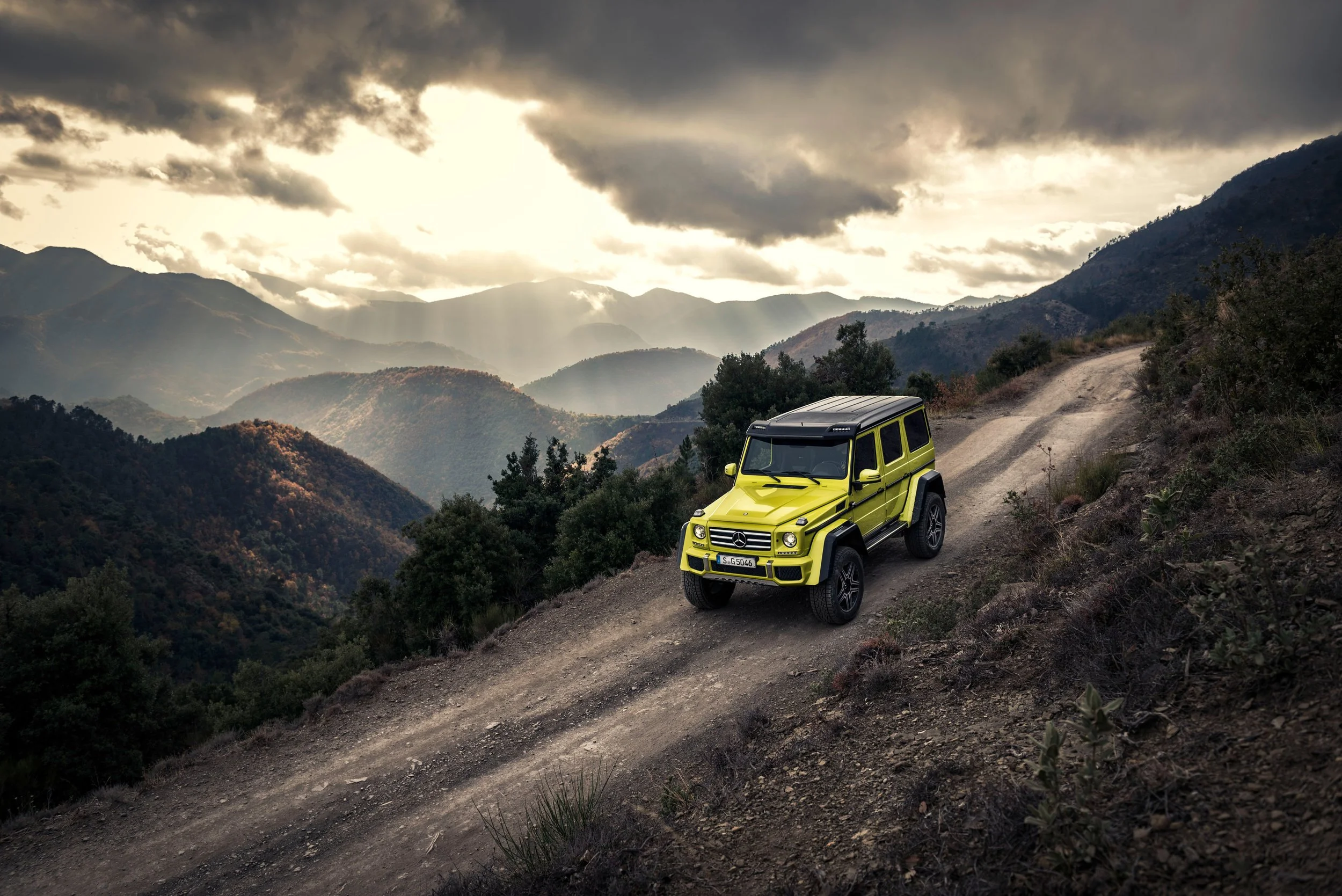 Neongelbe Mercedes G-Klasse 4x4 auf Bergpiste vor dramatischer Wolkenstimmung – High-End-Retusche von Bildergut.