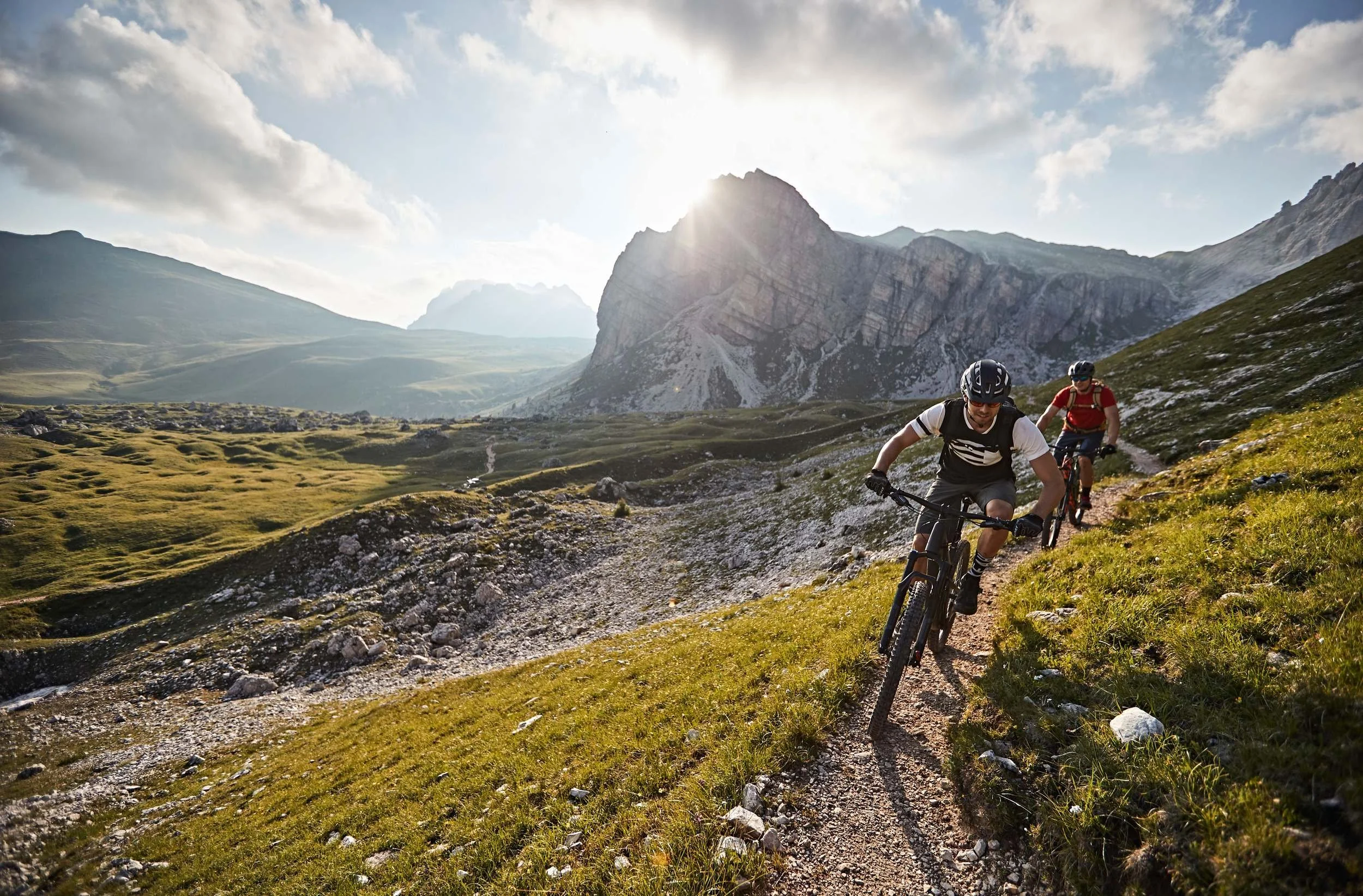Zwei Mountainbiker im Gegenlicht auf Dolomiten-Trail bei tiefstehender Sonne