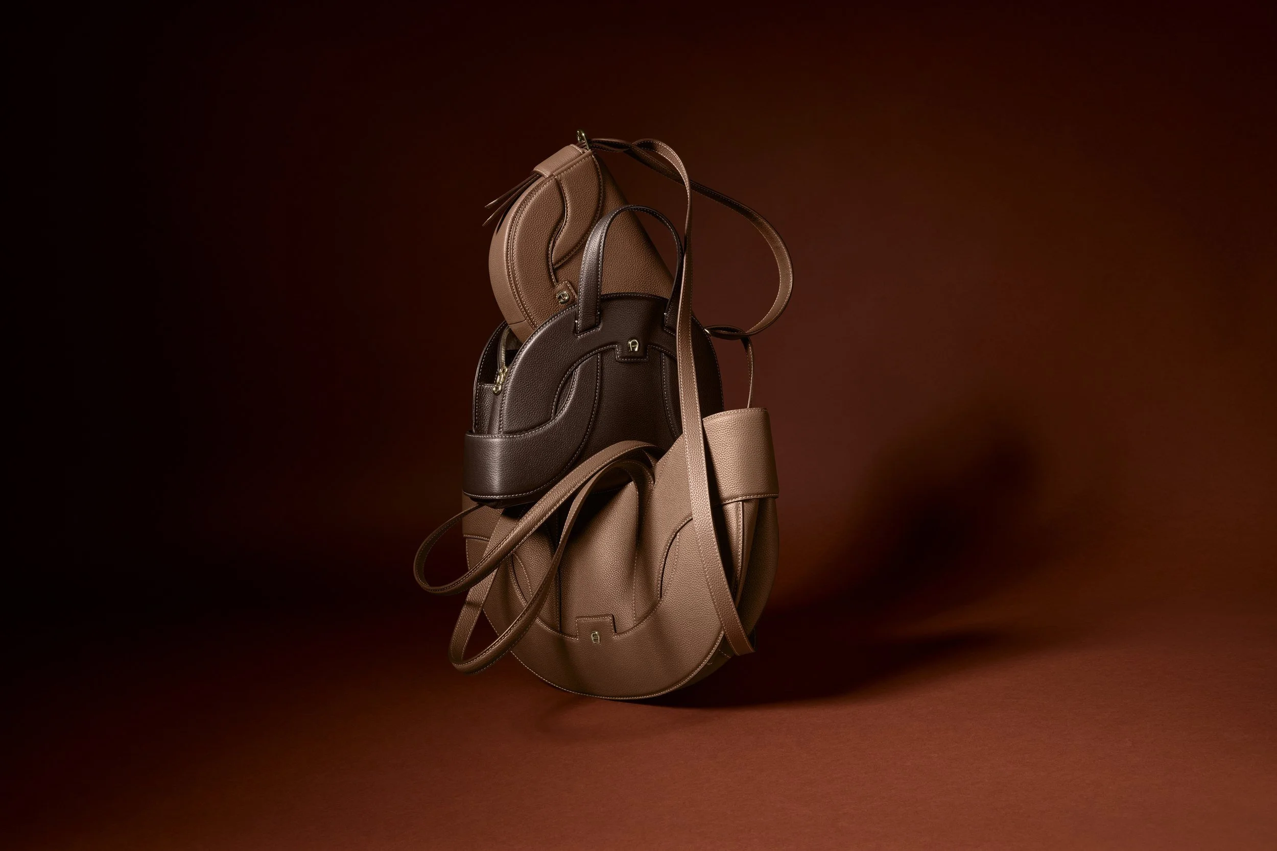 AIGNER Fall-Winter 2026: Sellina Satteltasche in Cognac vor braunem Grund