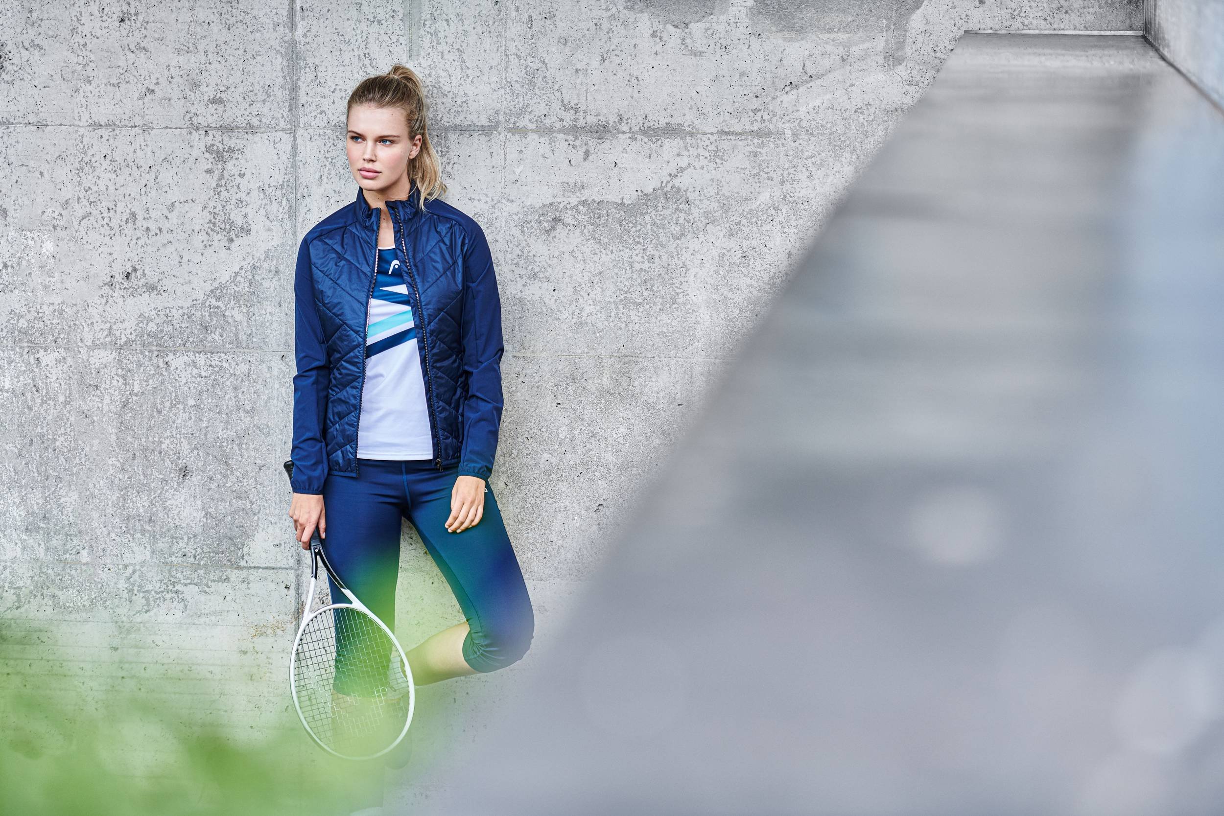 Spielerin mit Trainingsjacke und Schläger vor Beton