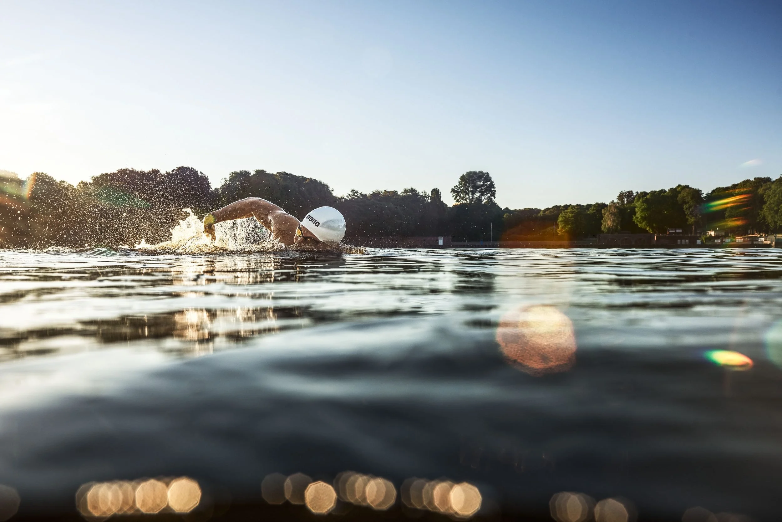 Schwimmer-Editorial von Tim Wendrich: Kraulzüge quer durchs Bild mit Lichtreflexen auf dem See