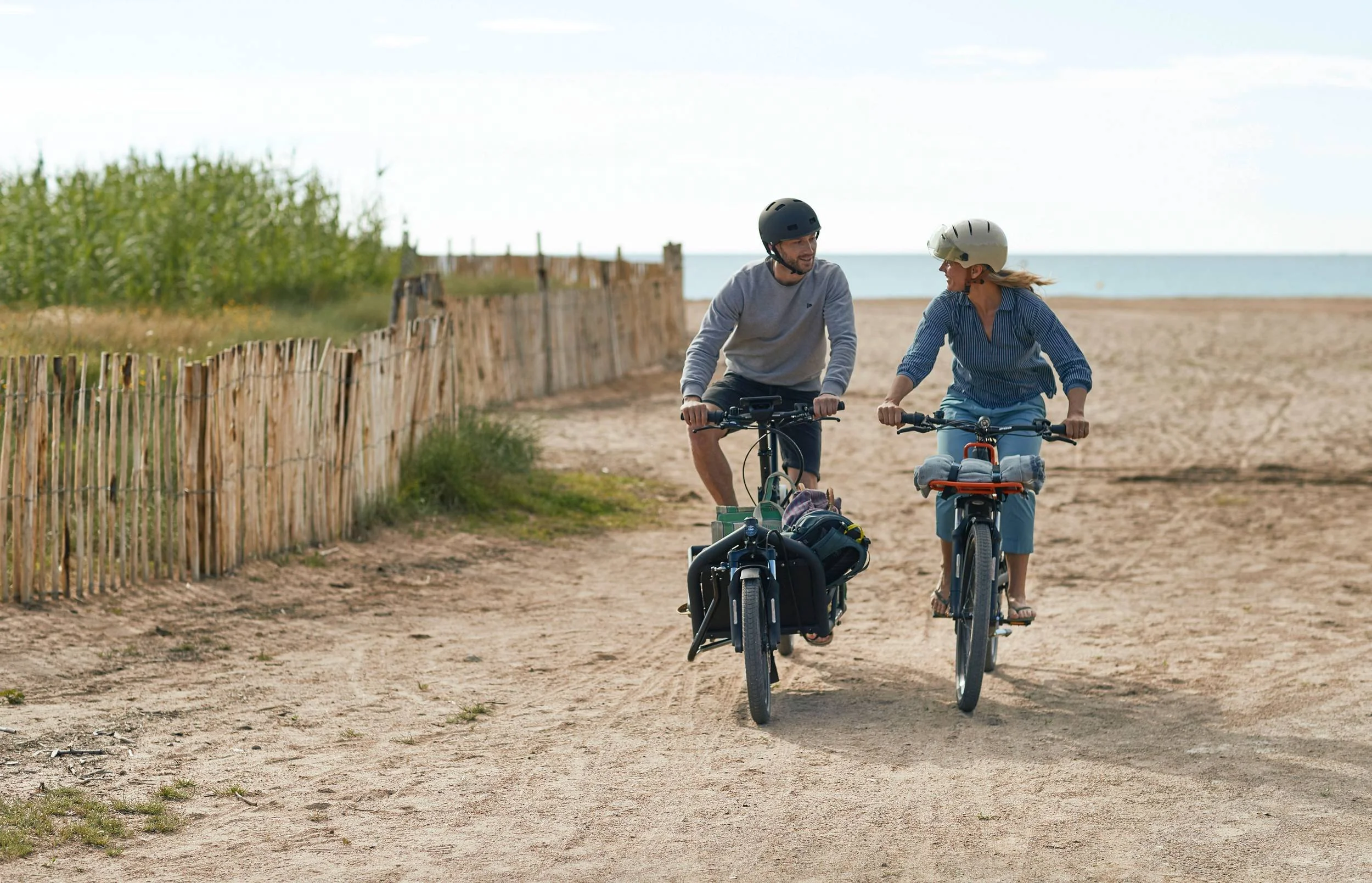 Paar fährt bepackte E-Bikes über Dünenweg am Meer