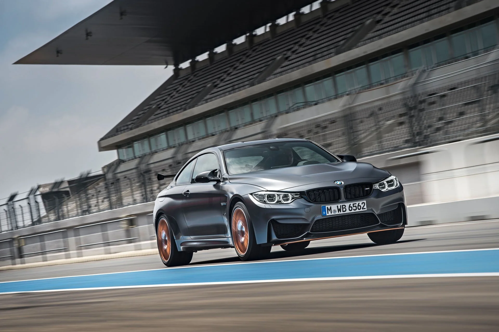 Grauer BMW M4 GTS mit orangefarbenen Felgen in Fahrt auf der Rennstrecke – High-End-Retusche von Bildergut.