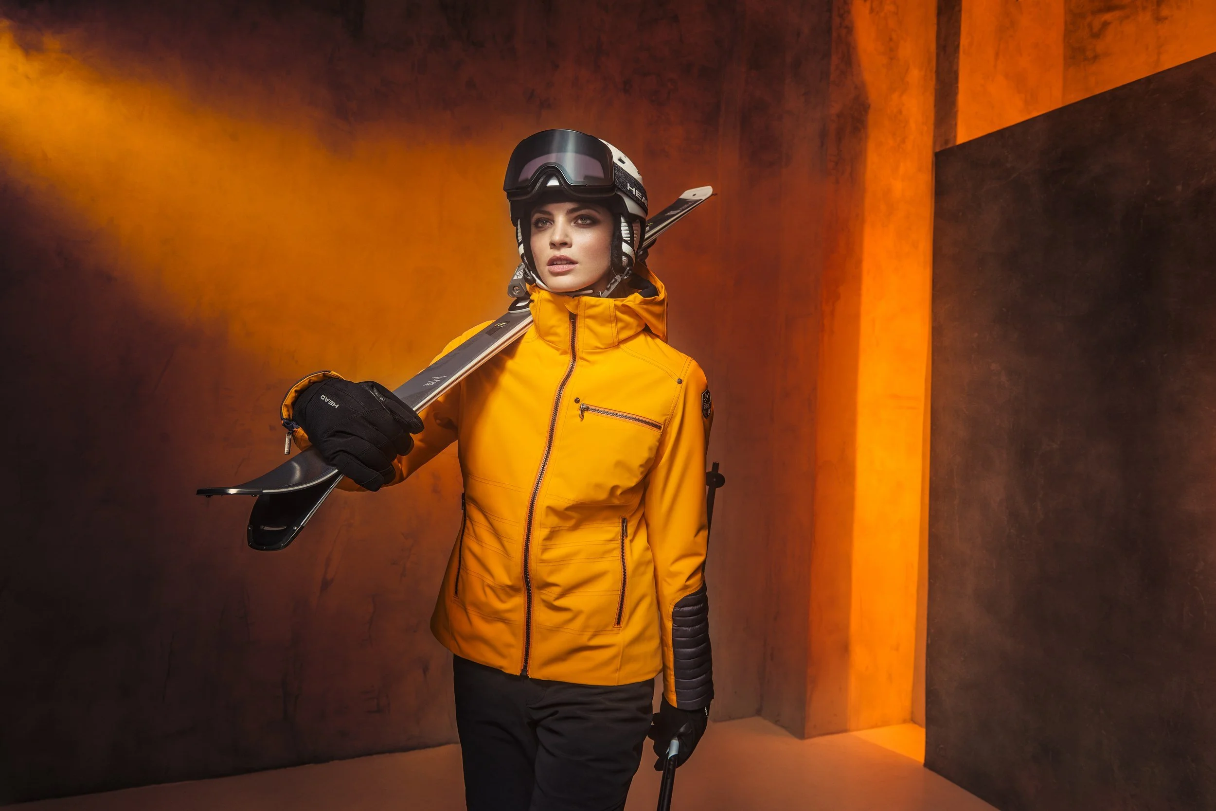 Skifahrerin in orangefarbener Jacke im Lichtkegel vor Betonkulisse