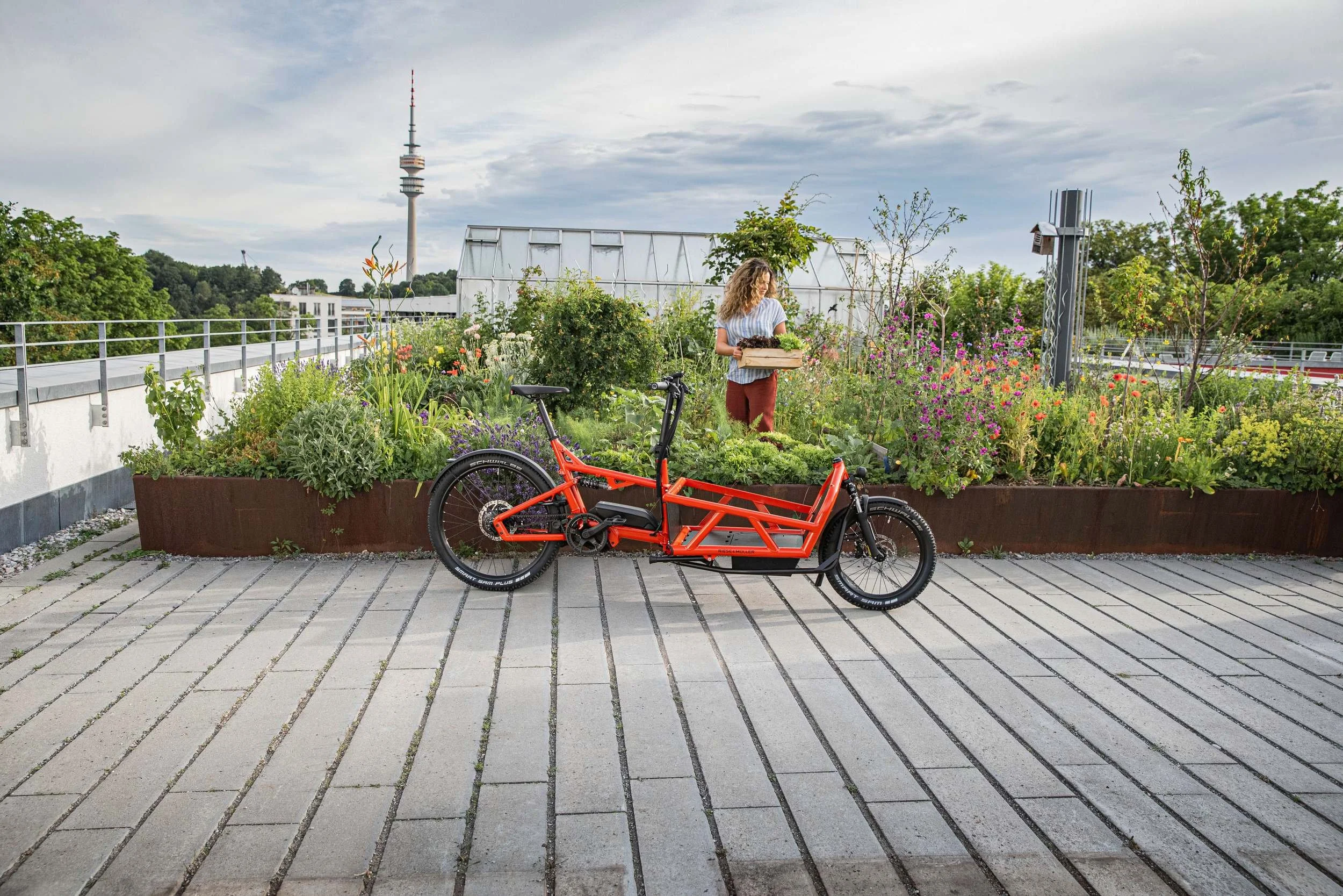Rotes Cargobike auf Dachterrasse, Münchner Olympiaturm im Hintergrund