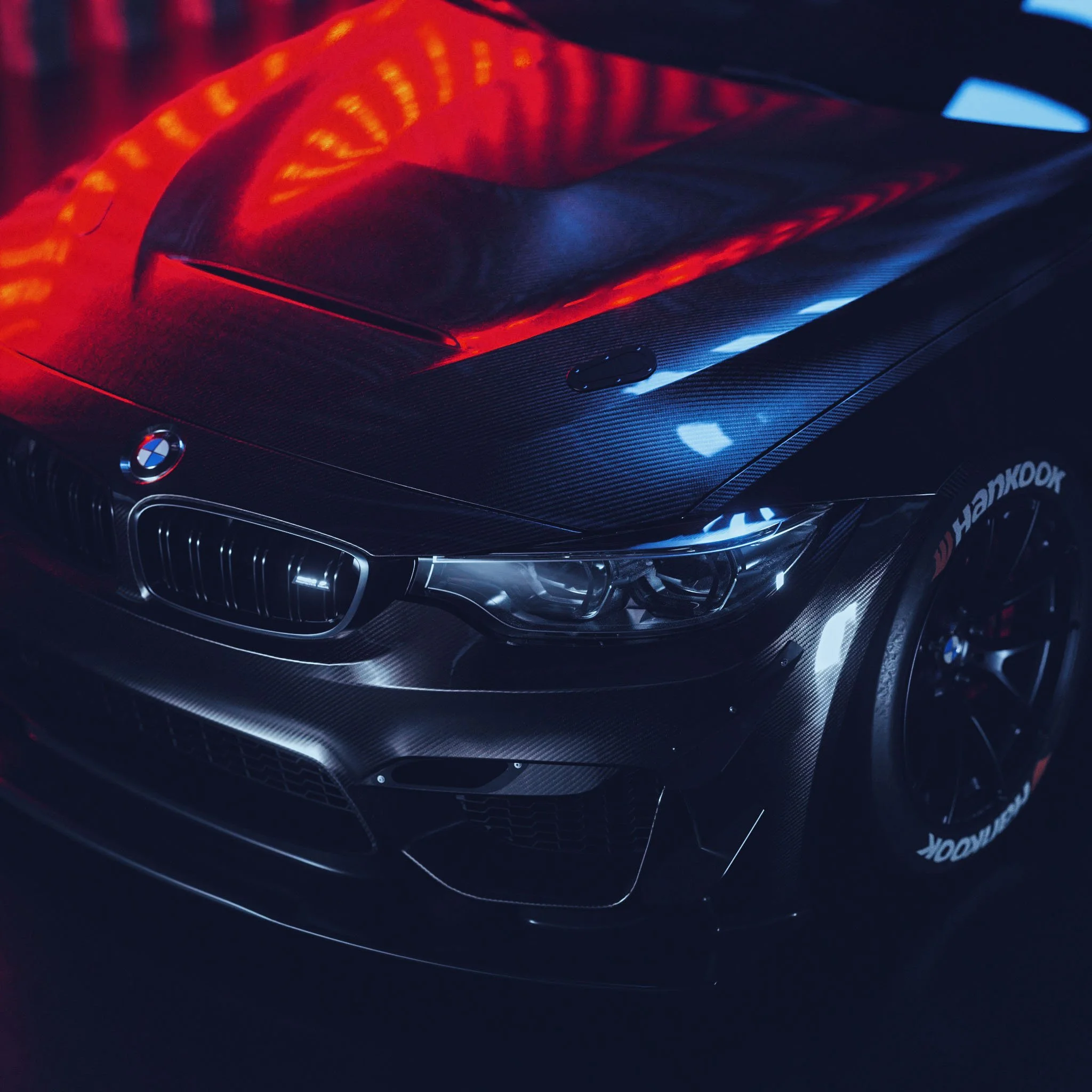 Schwarzer BMW M4 Rennwagen mit Carbonhaube in Nahaufnahme unter rot-blauem Licht – Retusche Bildergut.