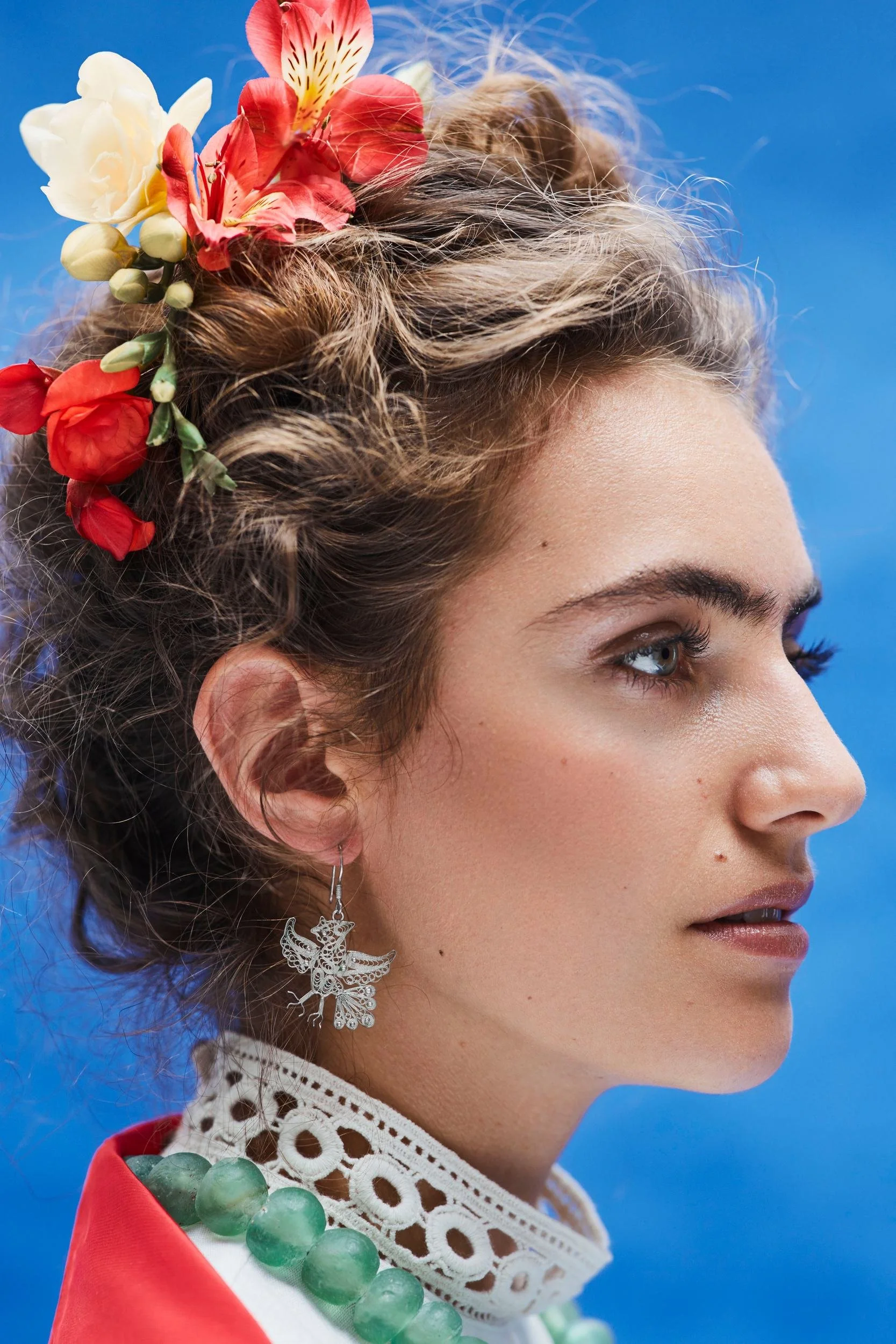 Profil mit Blumenkranz und Ohrring vor blauem Grund