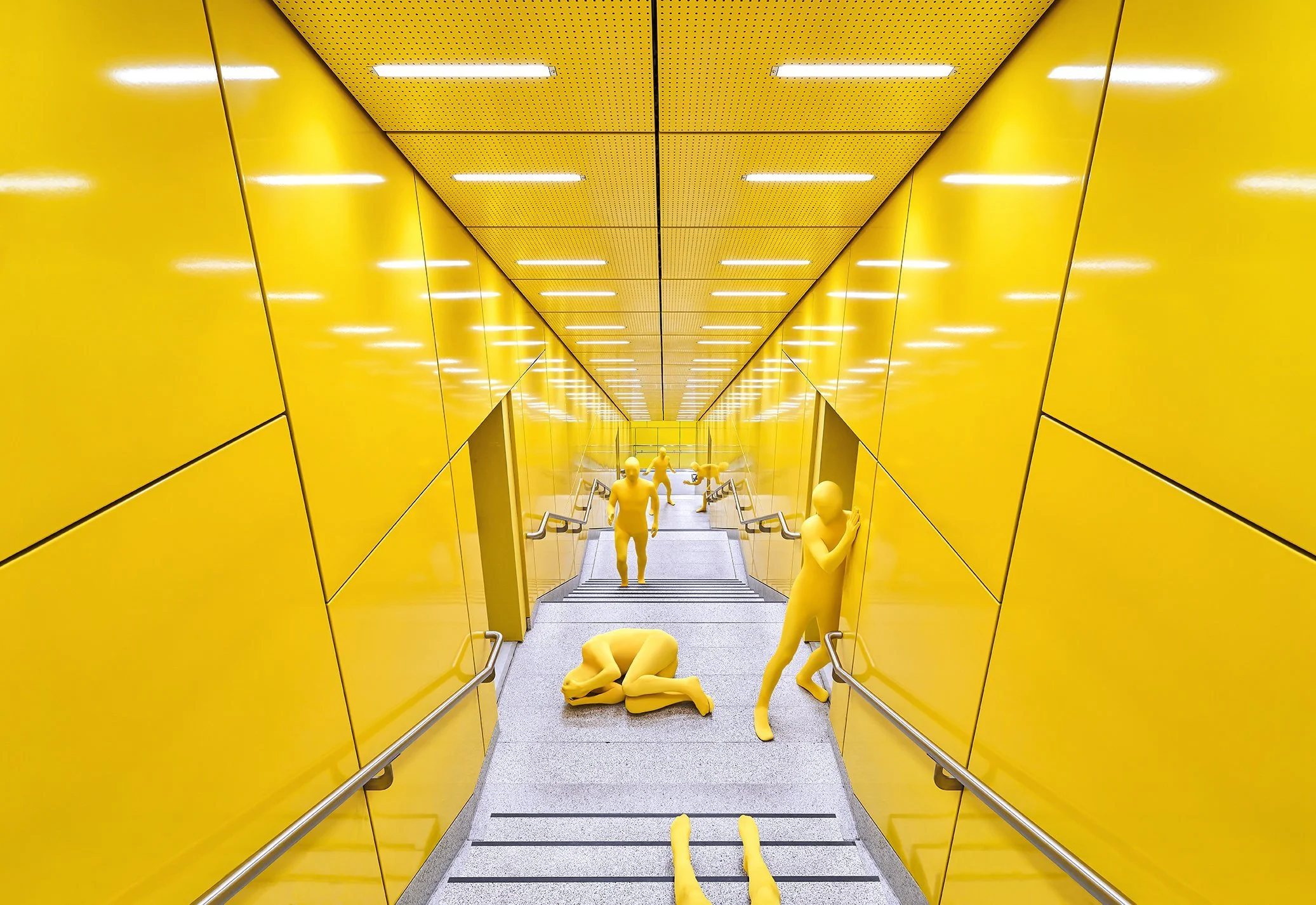 Gelbe Ganzkörperfiguren in leuchtend gelber U-Bahn-Passage, surreale Szene von Nick Frank – Composing Bildergut.
