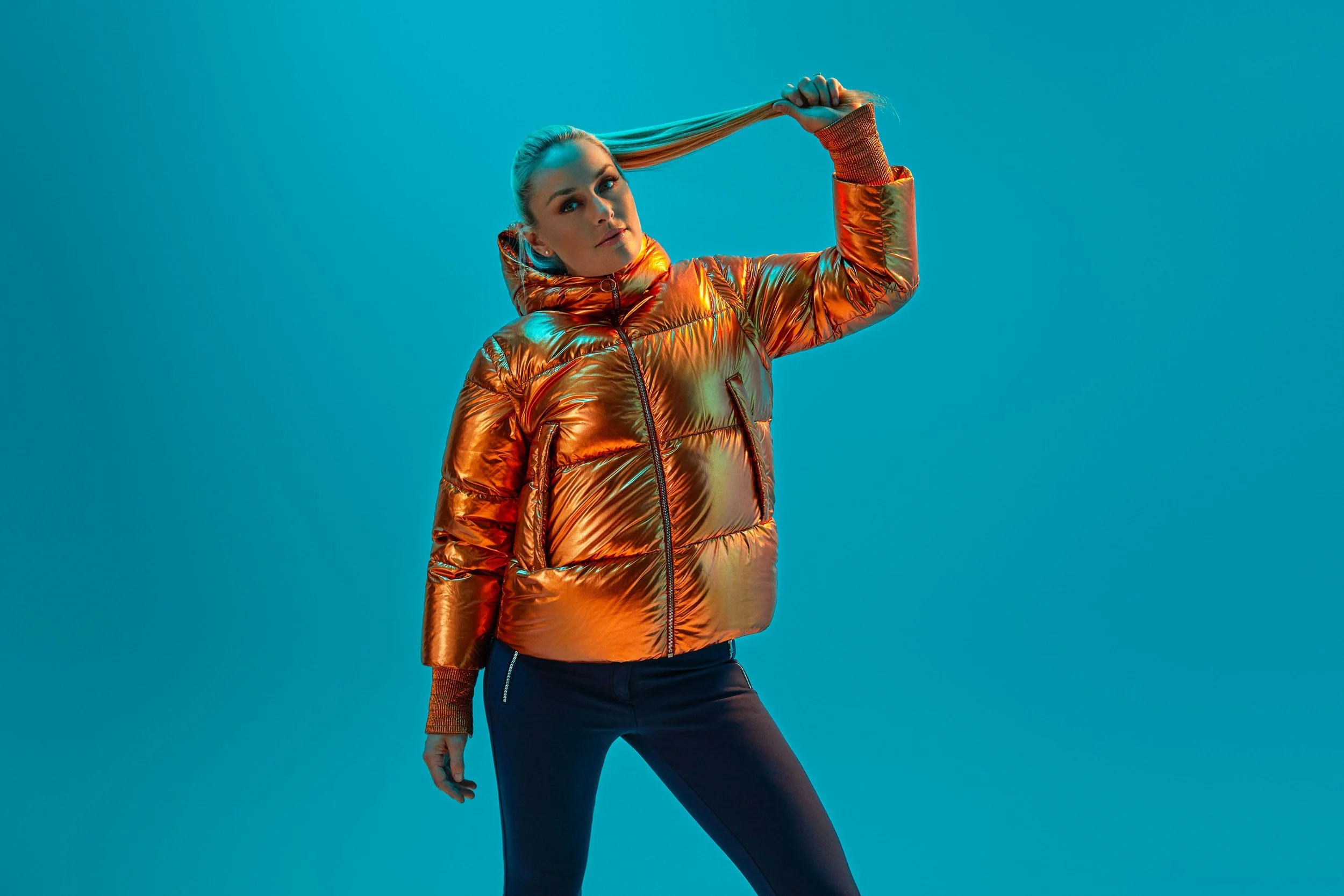 Pose in orangefarbener Metallic-Jacke vor Türkis