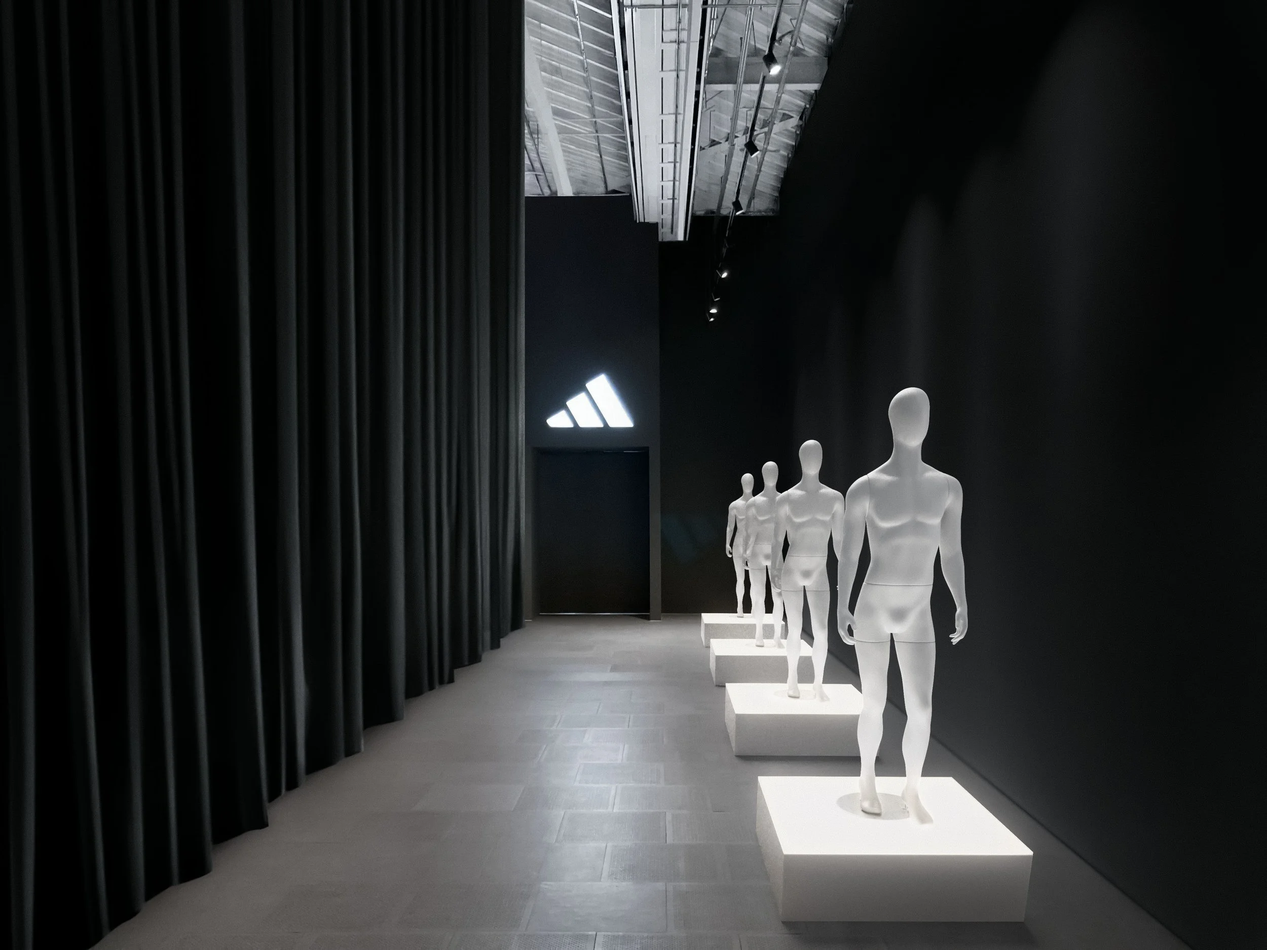 Weiße Schaufensterfiguren auf Podesten in dunklem Adidas Brand Space mit Logo – Retusche Bildergut.
