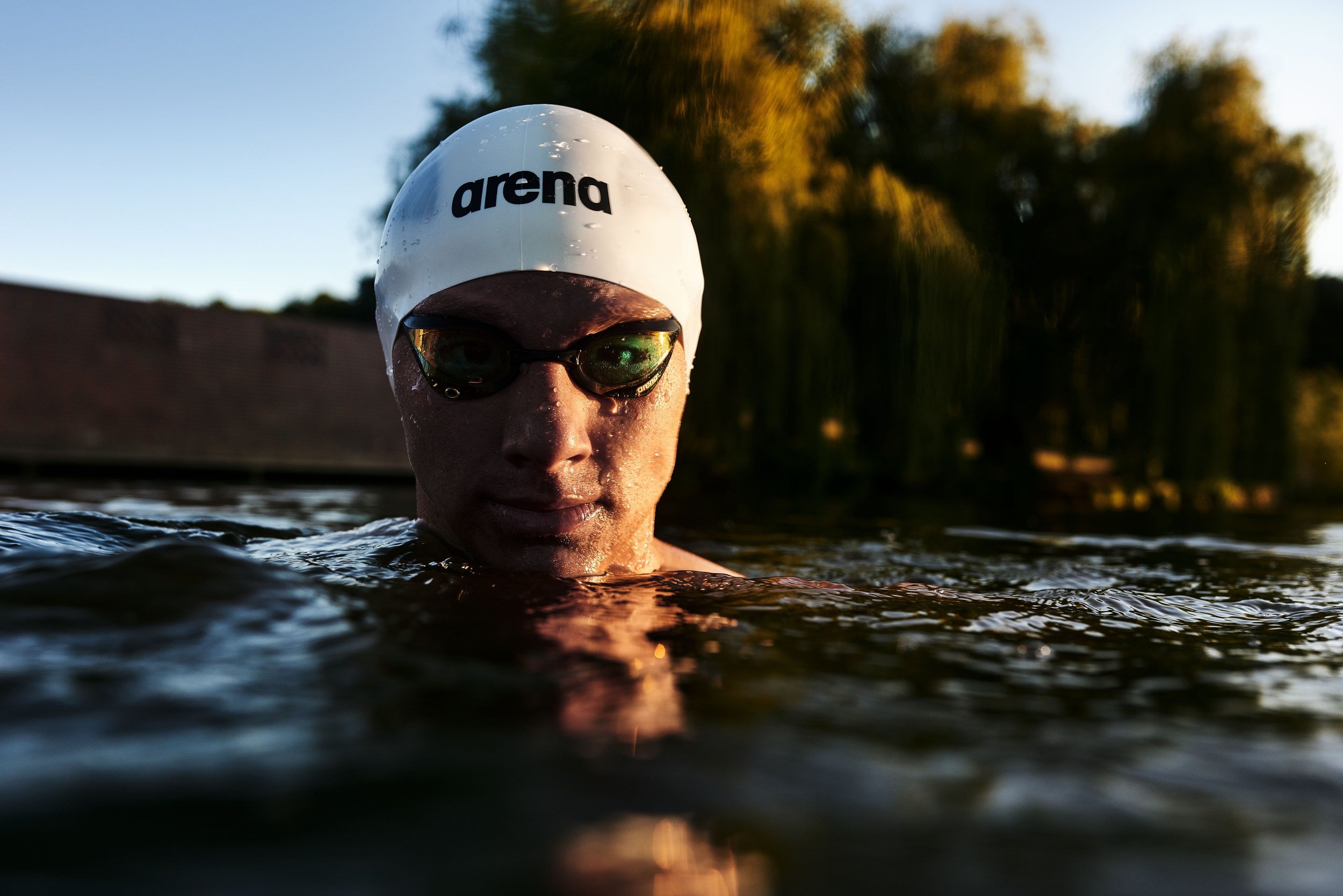 Schwimmer-Editorial von Tim Wendrich: halb aufgetauchtes Porträt mit dunkler Schwimmbrille vor Trauerweide