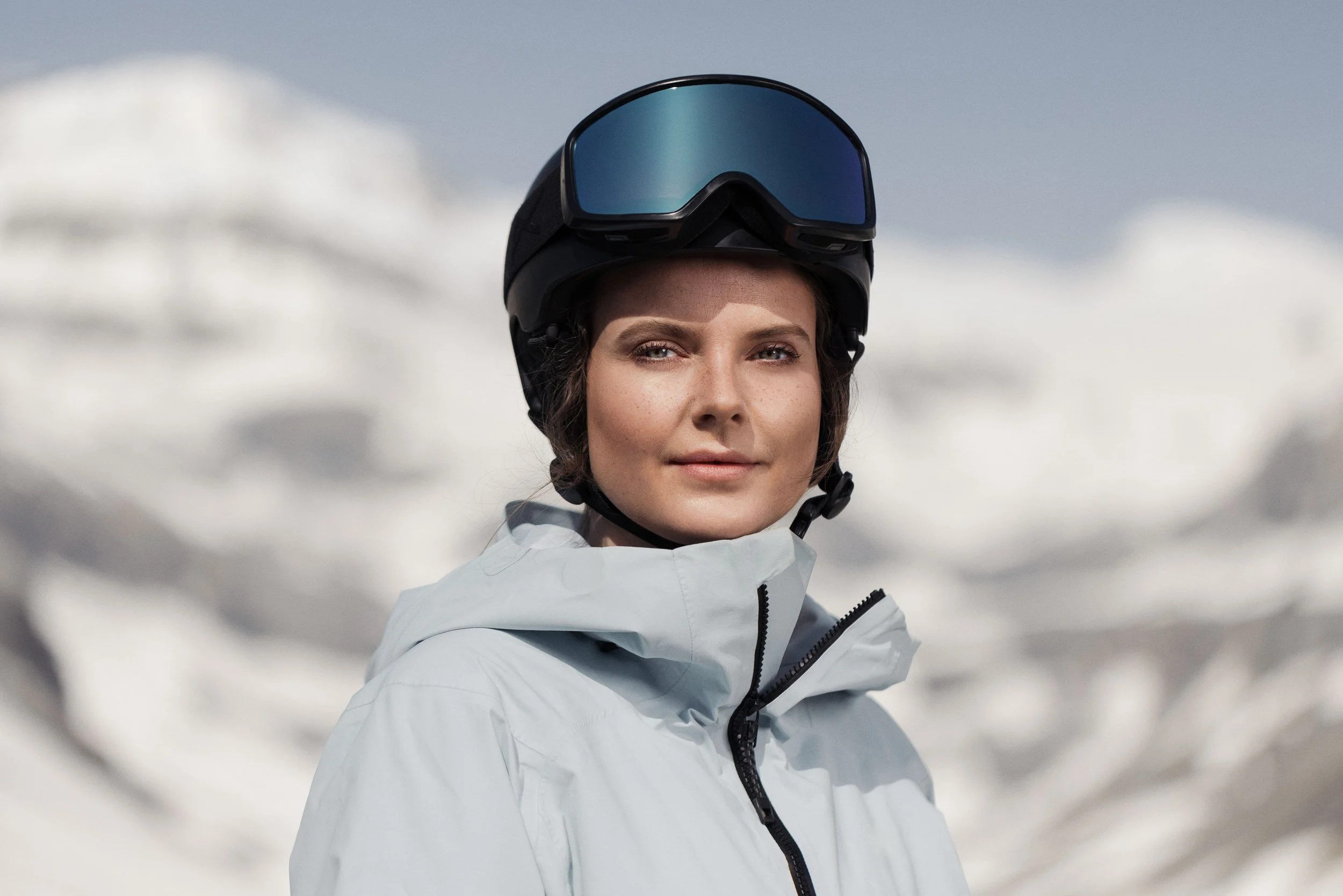 Skifahrerin in heller Jacke vor verschneiten Gipfeln
