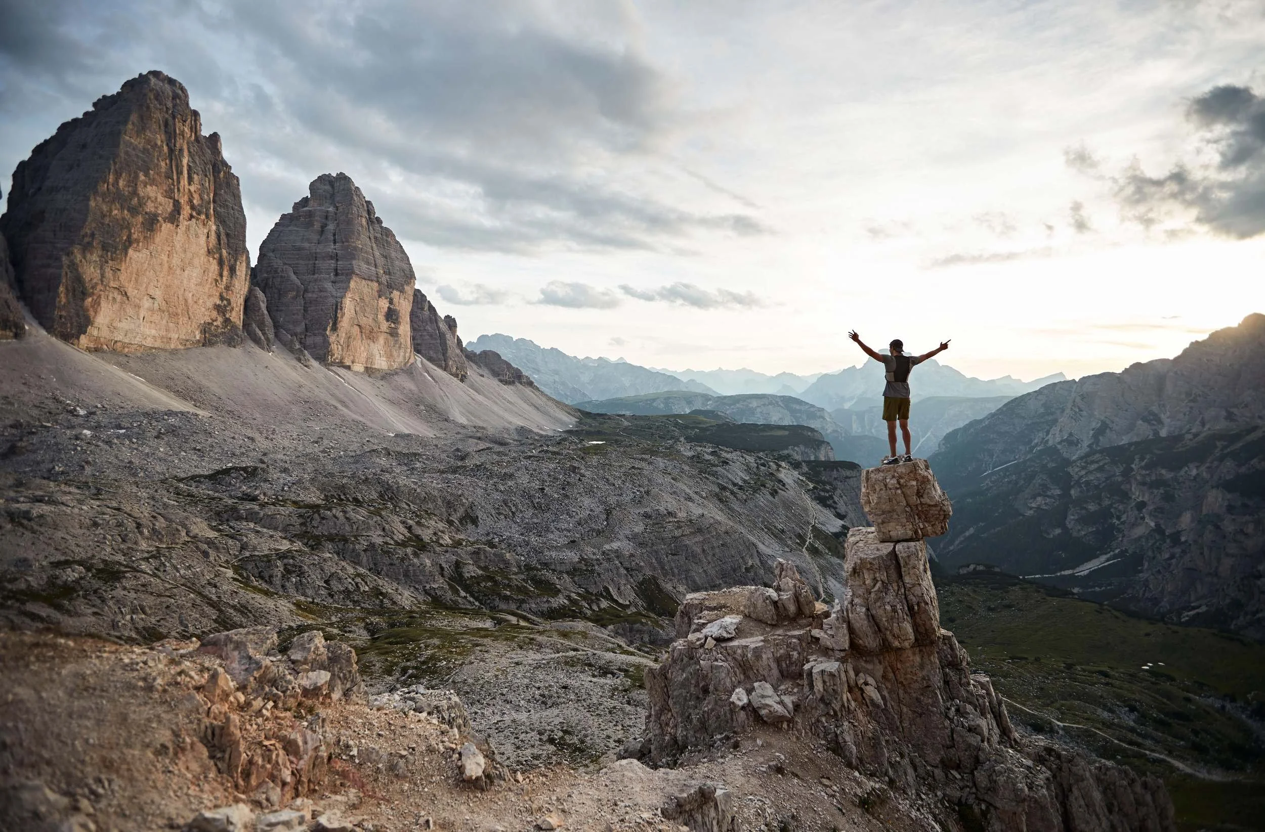 Trailrunner jubelt mit erhobenen Armen auf Felsturm im Dolomiten-Panorama