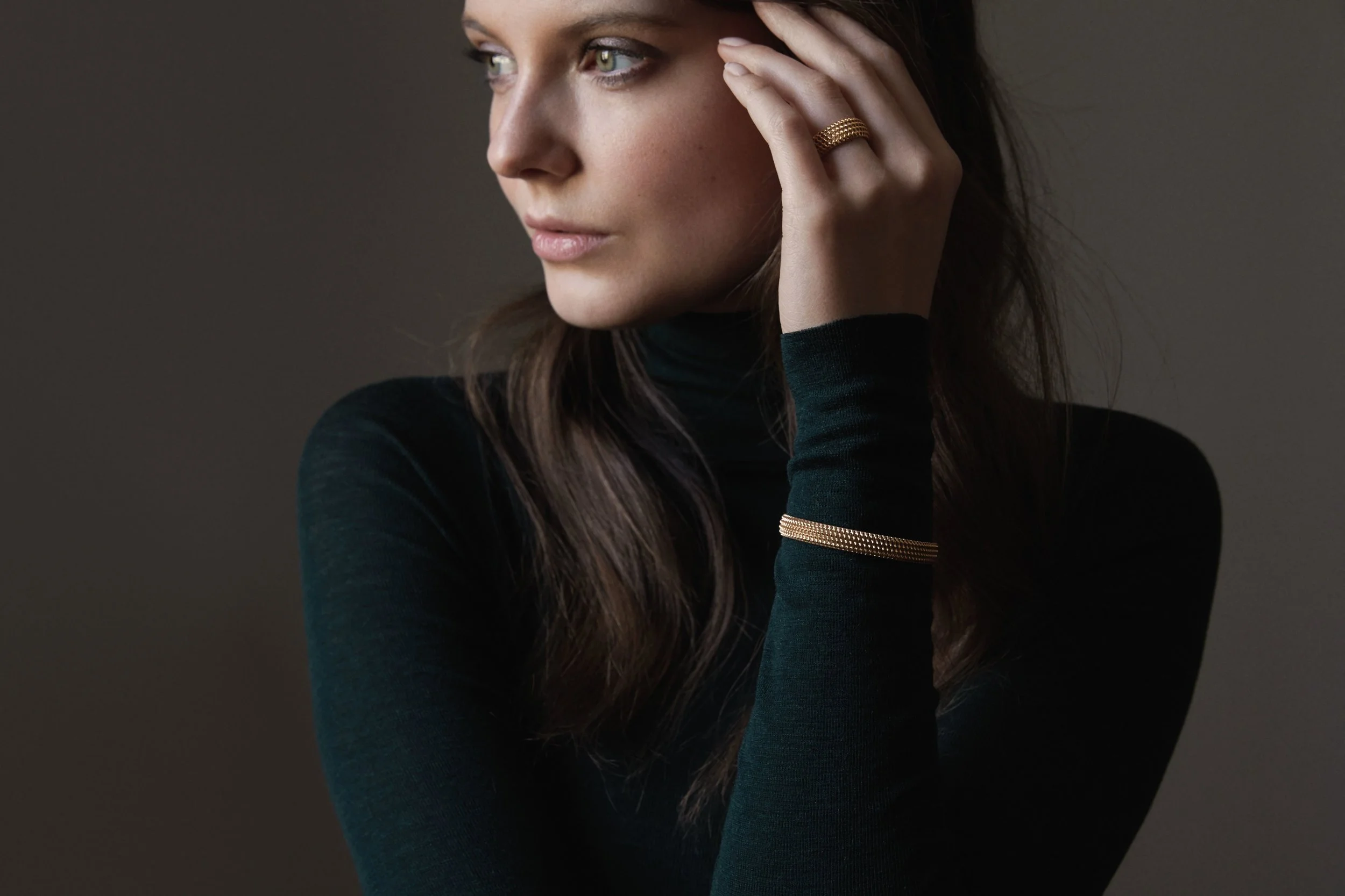 Hände mit Goldring an dunklem Kleid vor schwarzem Grund, Schmuck-Editorial für Sian Design – Retusche Bildergut.