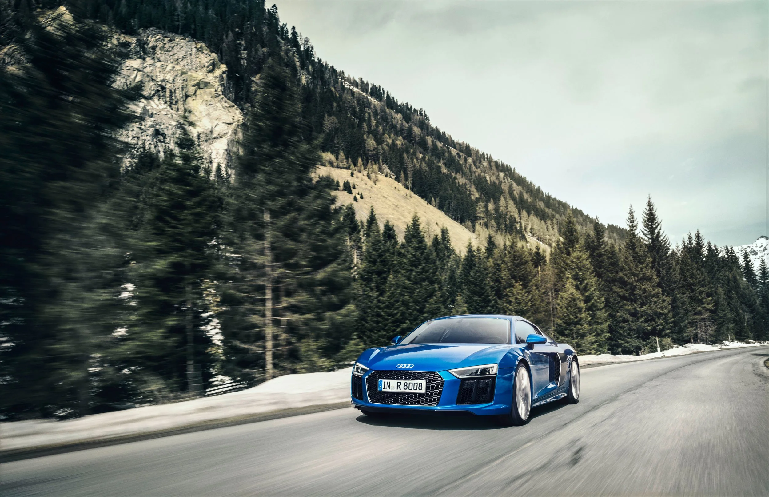 Blauer Audi R8 in Fahrt durch Bergtunnel mit Schneelandschaft im Hintergrund – Retusche Bildergut.