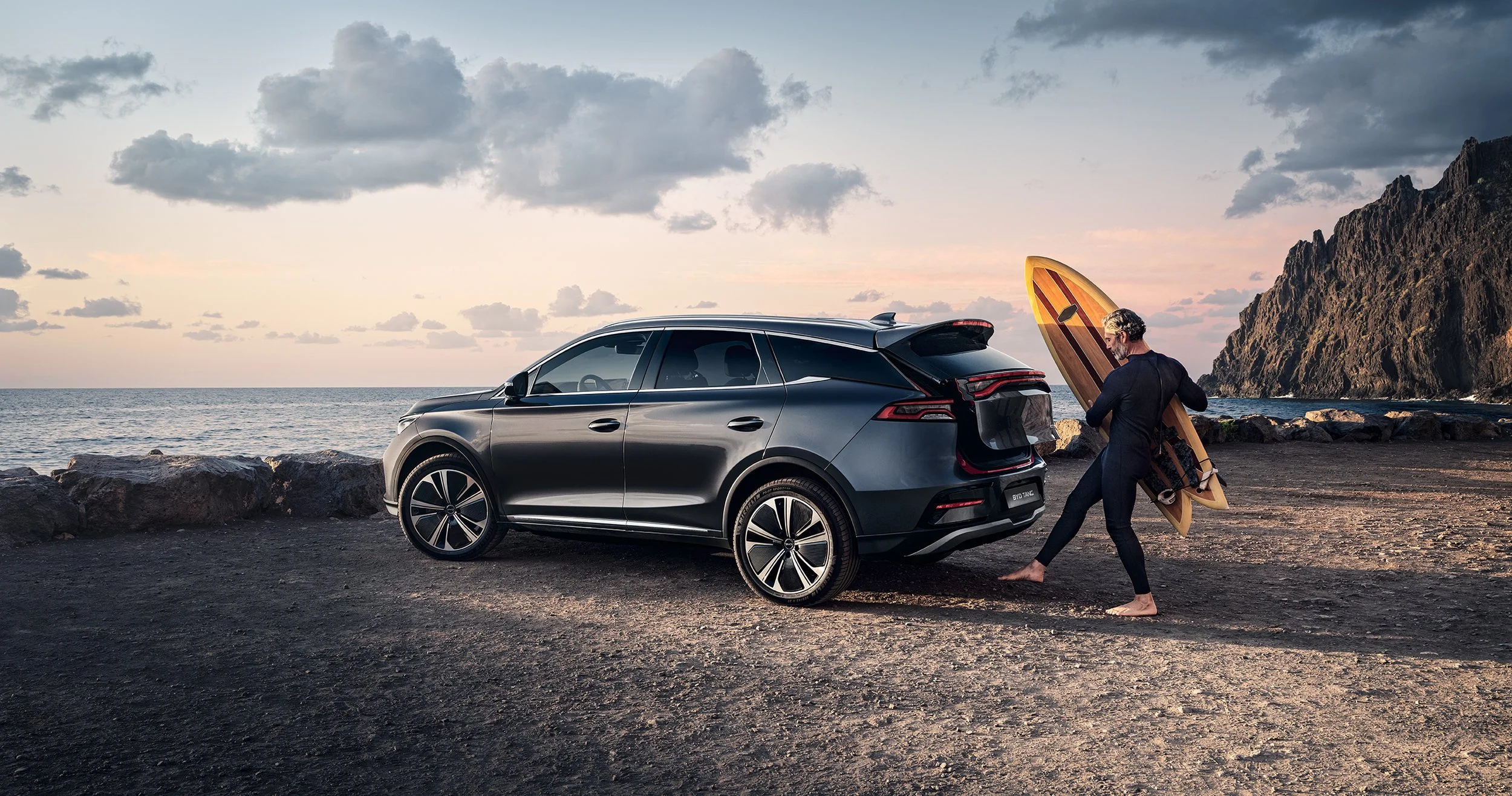Grauer BYD Tang mit Surfer am Meer bei Dämmerung vor Felsküste – Retusche Bildergut.