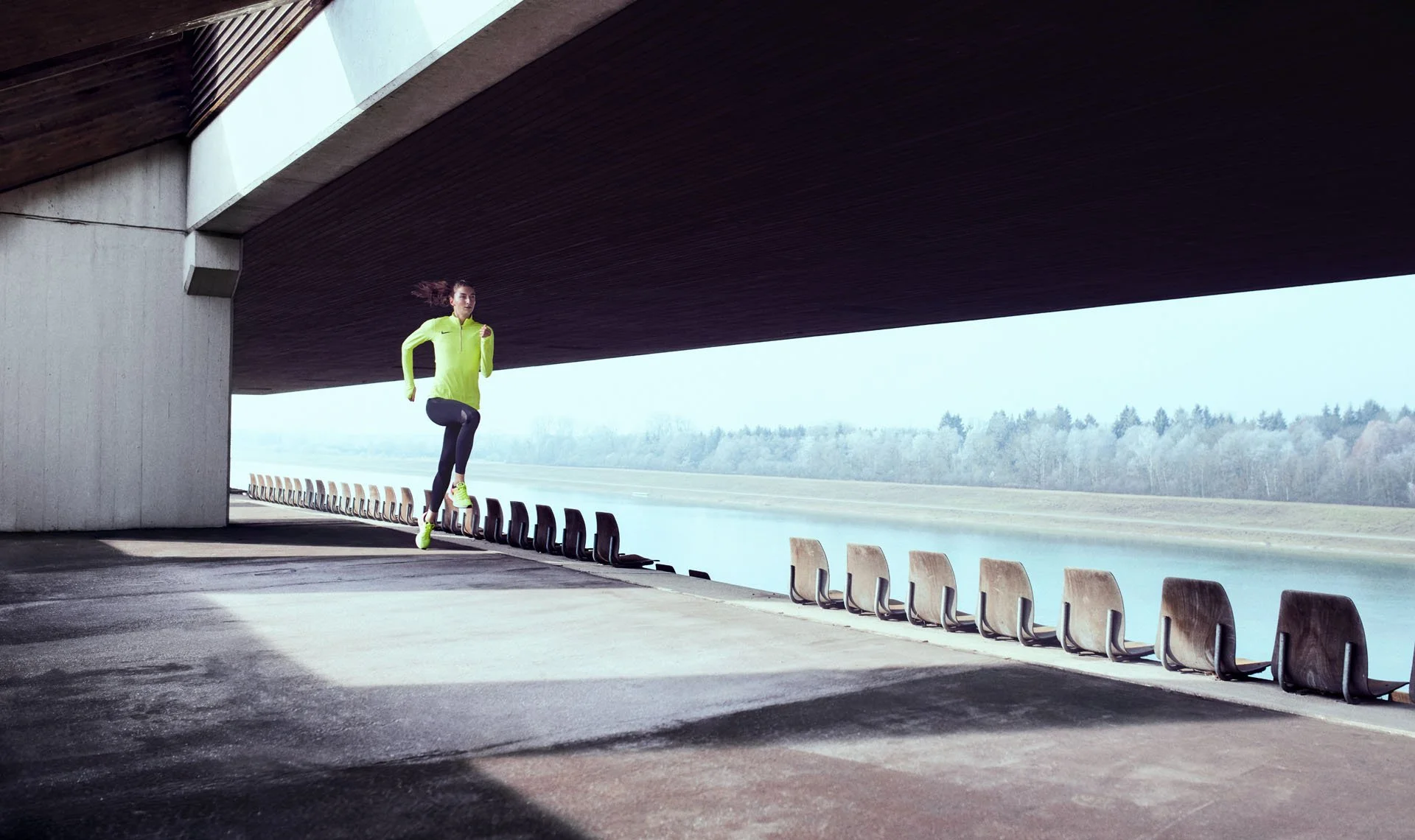Läuferin in neongelbem Top joggt unter einer Betonbrücke im Gegenlicht, Christina Hering Lookbook – Retusche Bildergut.