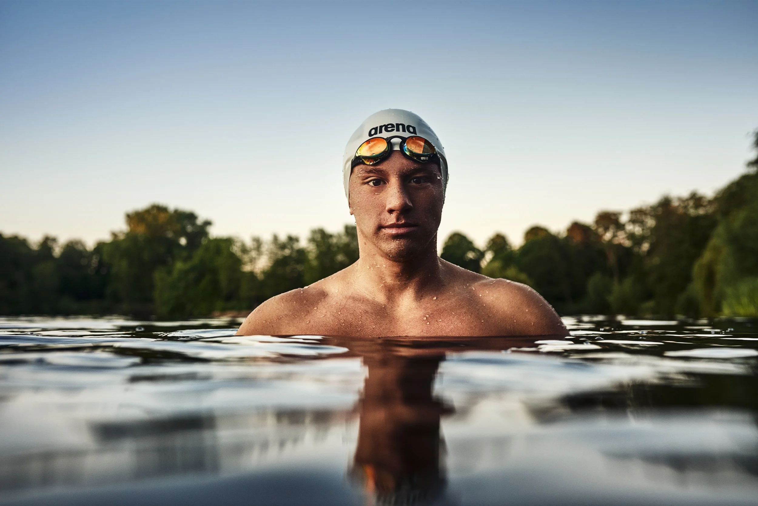 Schwimmer-Editorial von Tim Wendrich: frontales Porträt im See mit weißer Badekappe, Spiegelung im Abendlicht