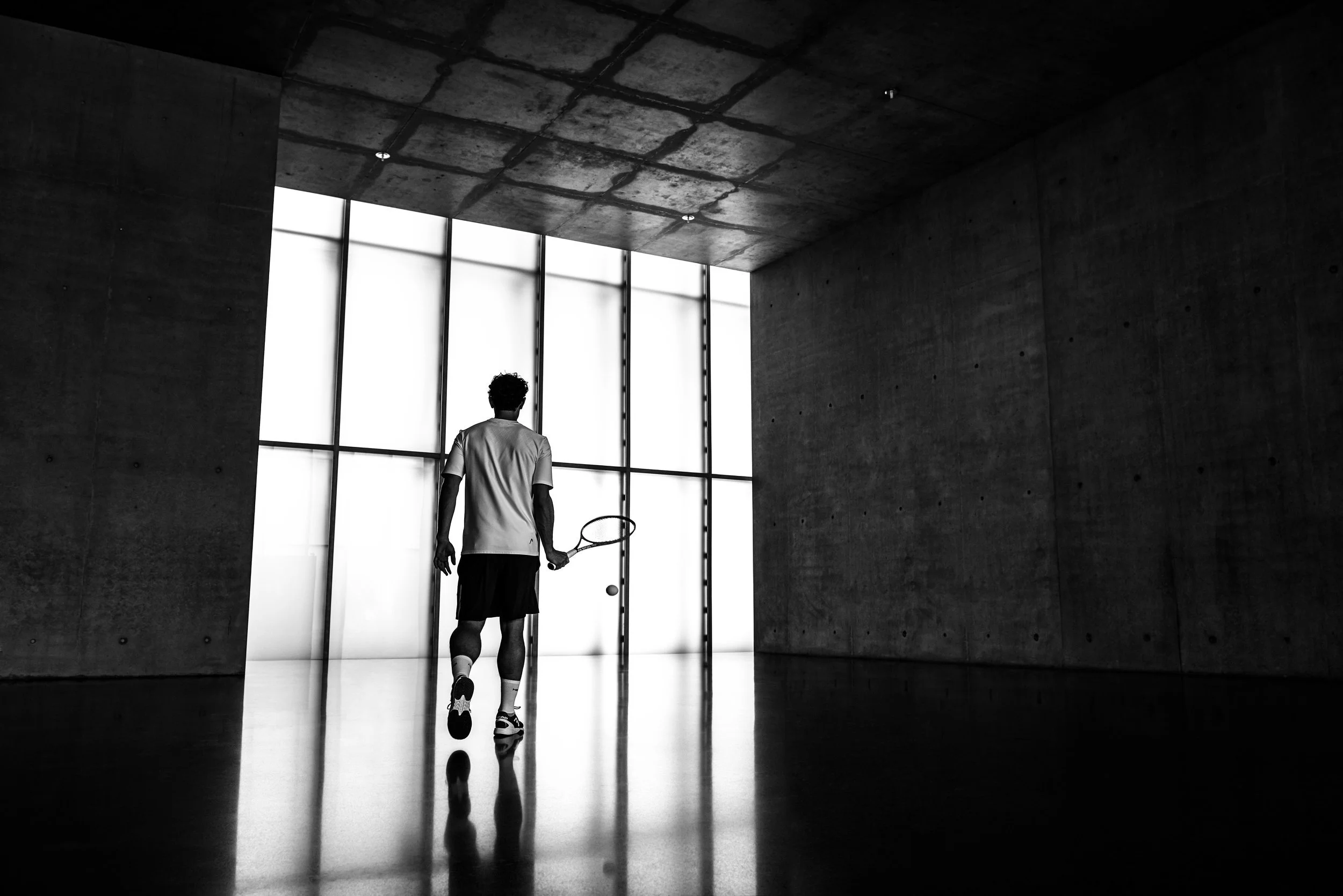 Squashspieler als Silhouette vor Lichtwand in Betonhalle, dramatisches Schwarz-Weiß für Head – Retusche Bildergut.