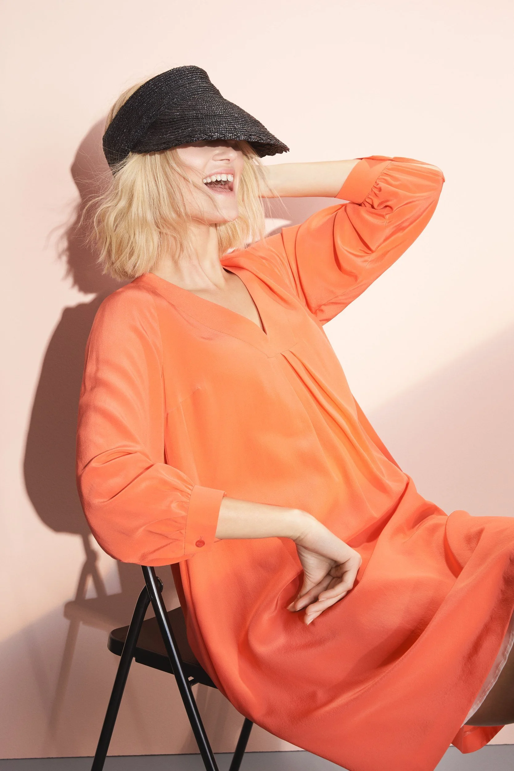 Hellmuth Lookbook SS20: Kleid DALLAS in Flamingo-Orange mit schwarzer Kappe, sitzende Pose