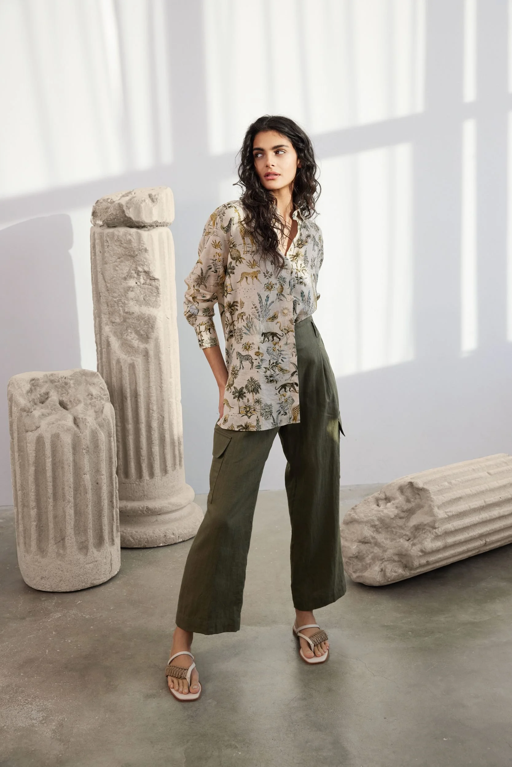 Modehaus Zinser Frühjahr-Sommer 2024: gemusterte Bluse zu olivgrüner Hose vor Säule und Vorhang