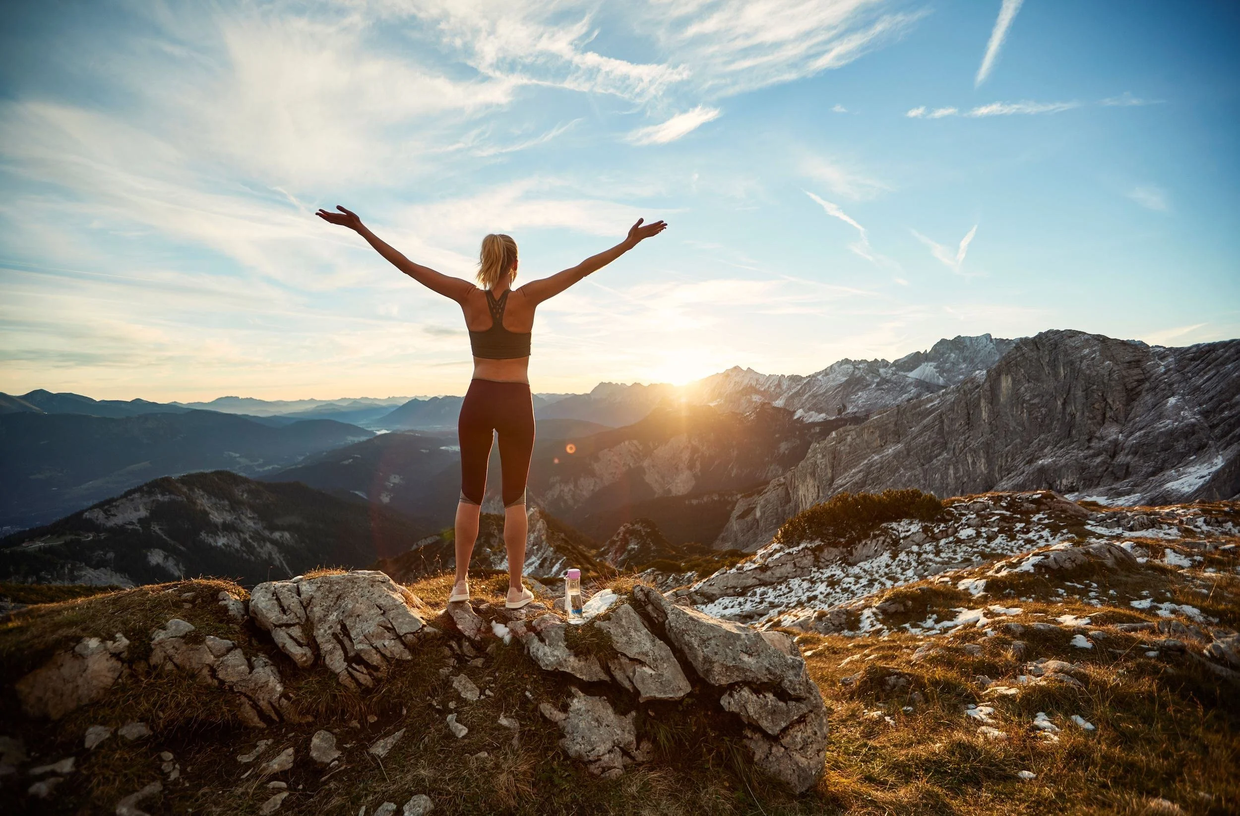 Frau mit ausgebreiteten Armen auf Berggipfel bei Sonnenaufgang