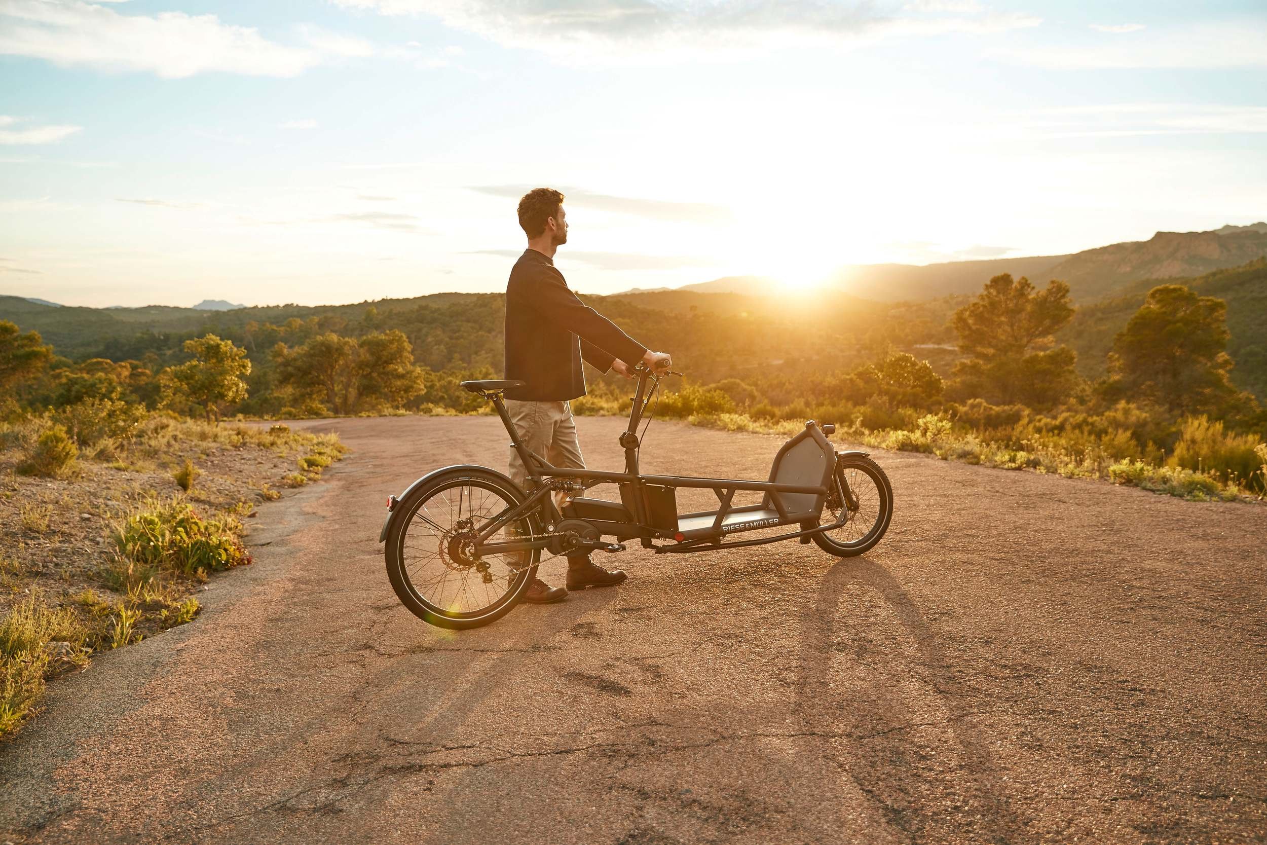 Silhouette eines Mannes mit Lastenrad im Gegenlicht der Abendsonne