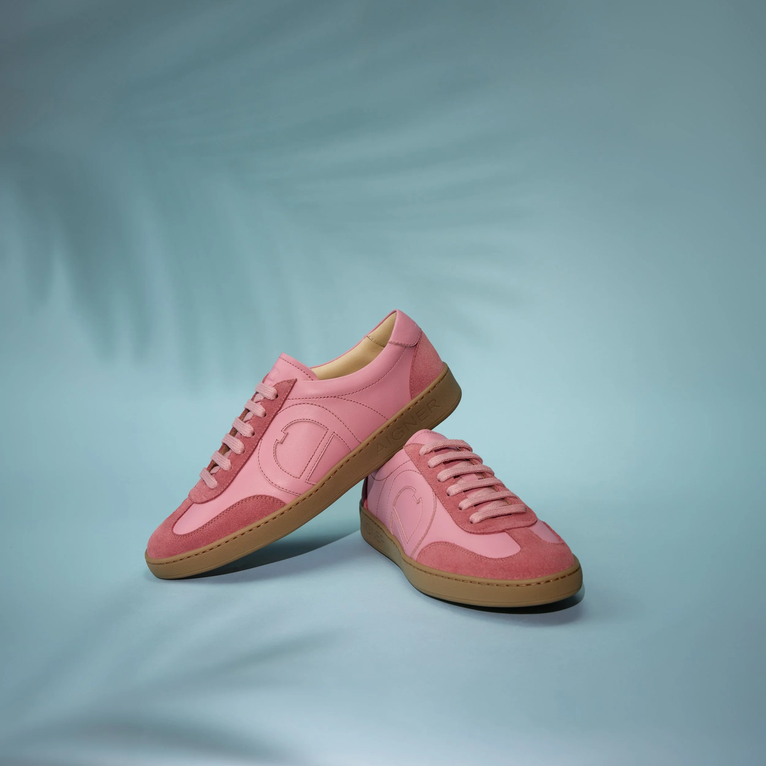 AIGNER Fall-Winter 2026: rosafarbener Ledersneaker vor türkisem Grund mit Palmenschatten