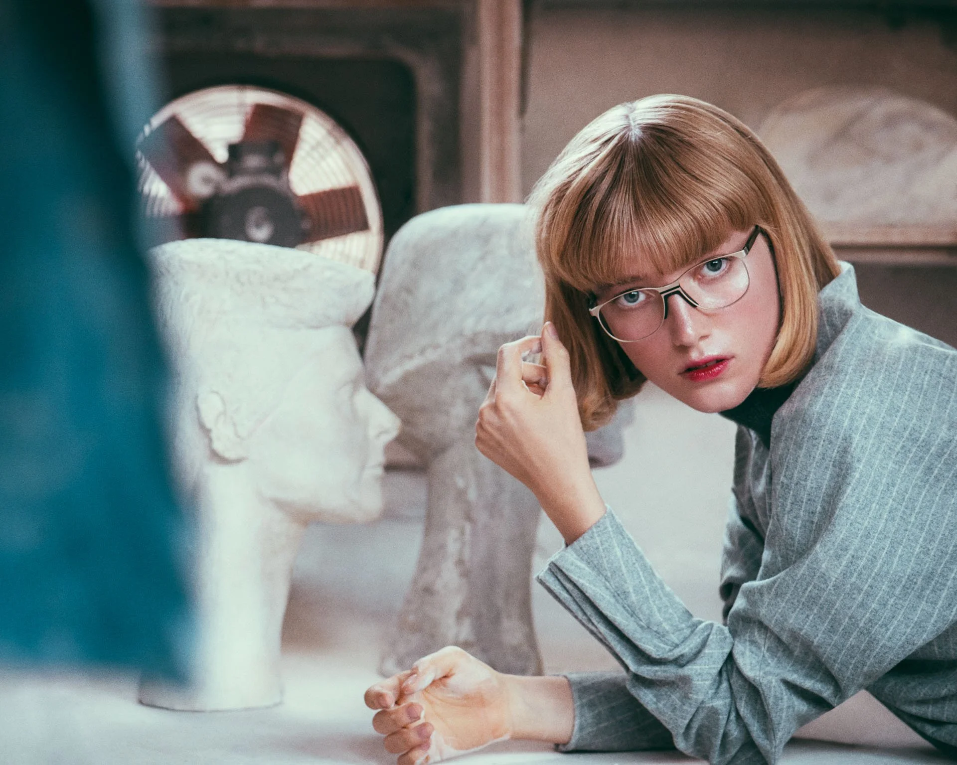 Andy Wolf White Heat, Modell mit Brille im Bildhauer-Atelier neben Gipsbuesten