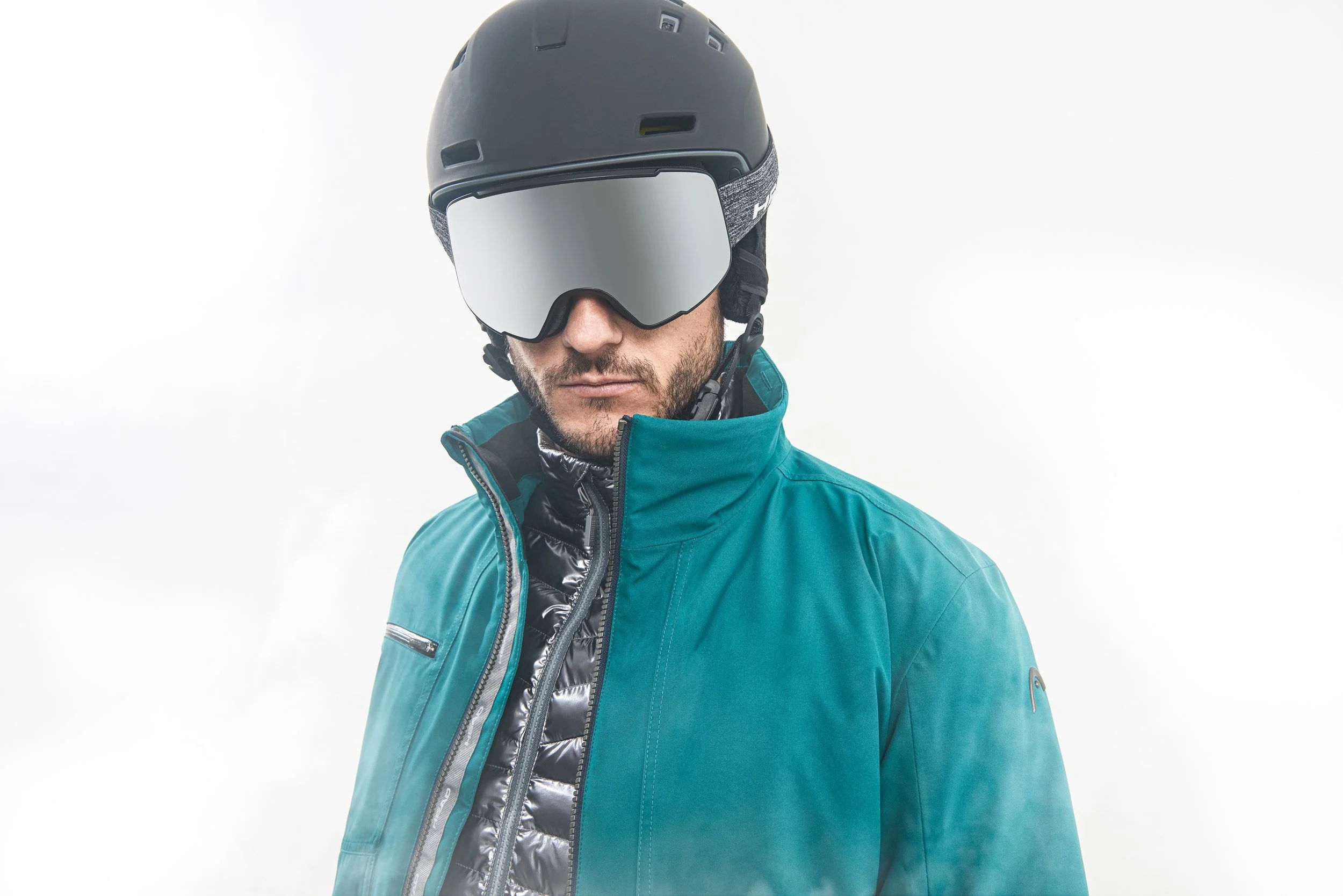 Skifahrer mit Helm und Brille in türkiser Jacke