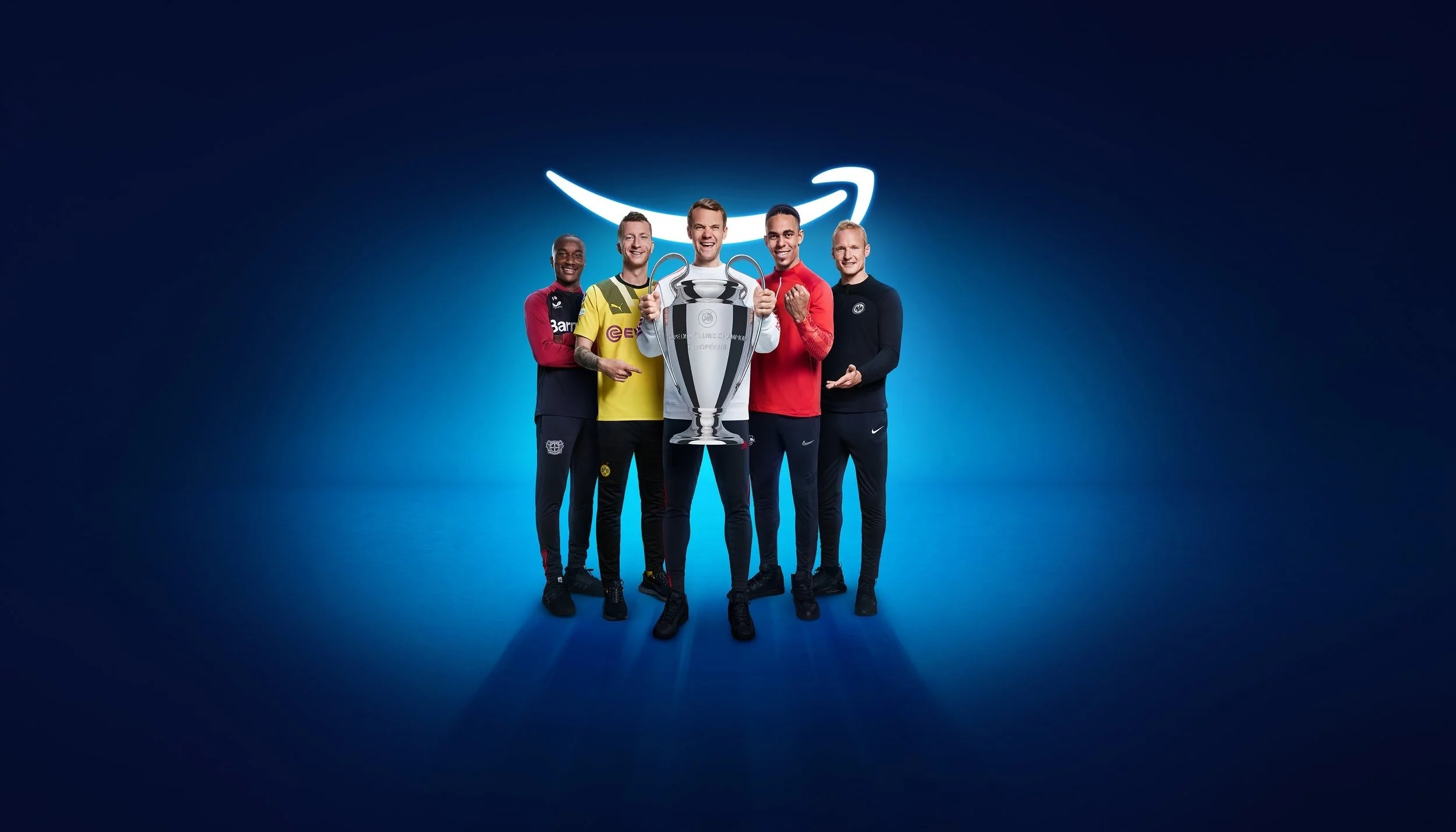 Fünf Fußballstars mit Champions-League-Pokal vor blauem Amazon-Smile, Amazon Prime UEFA Champions League – Composing Bildergut.