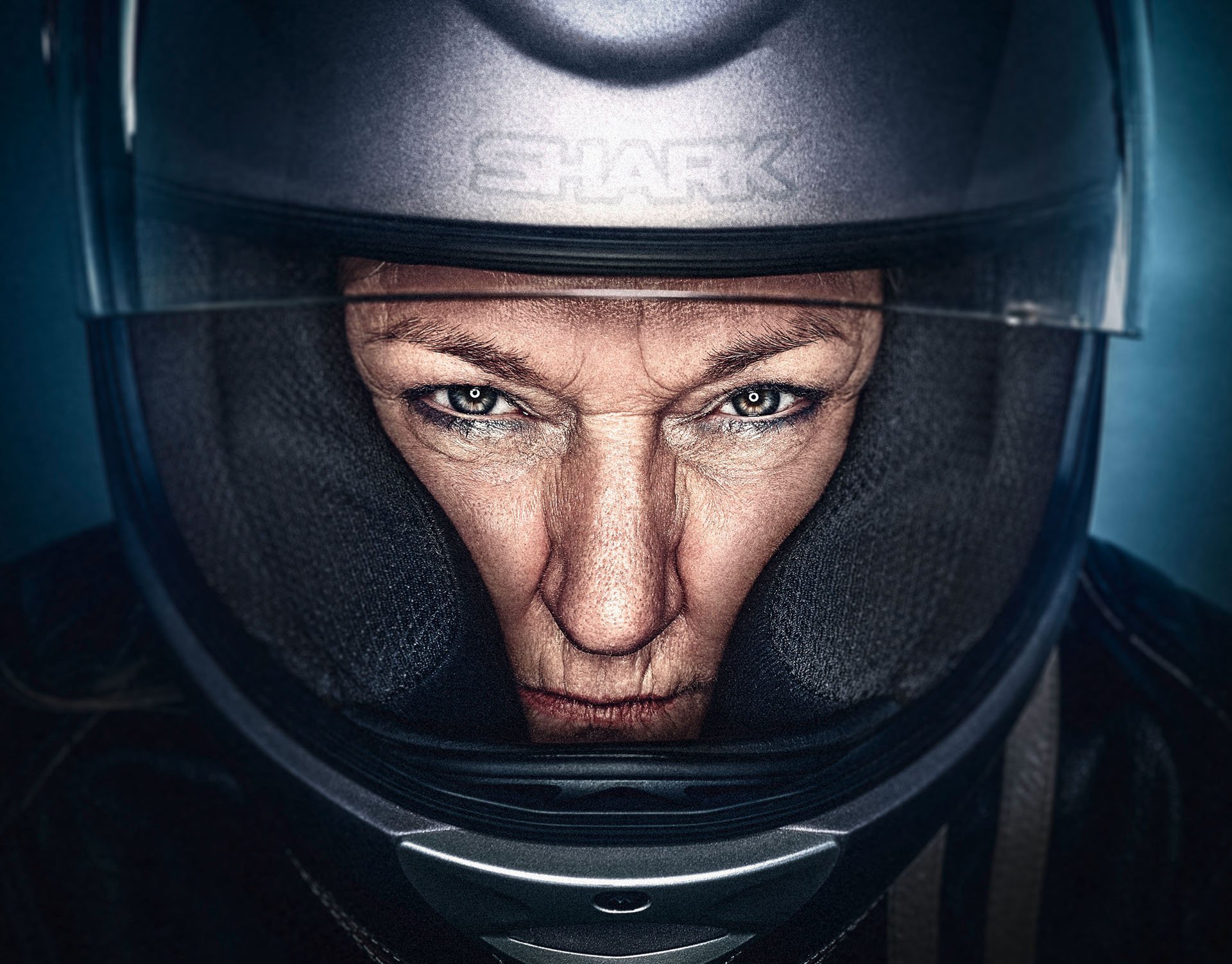 Motorradfahrer mit schwarz-rotem Shoei-Integralhelm, intensiver Blick in dunkelblauem Licht – Beauty-Retusche Bildergut.