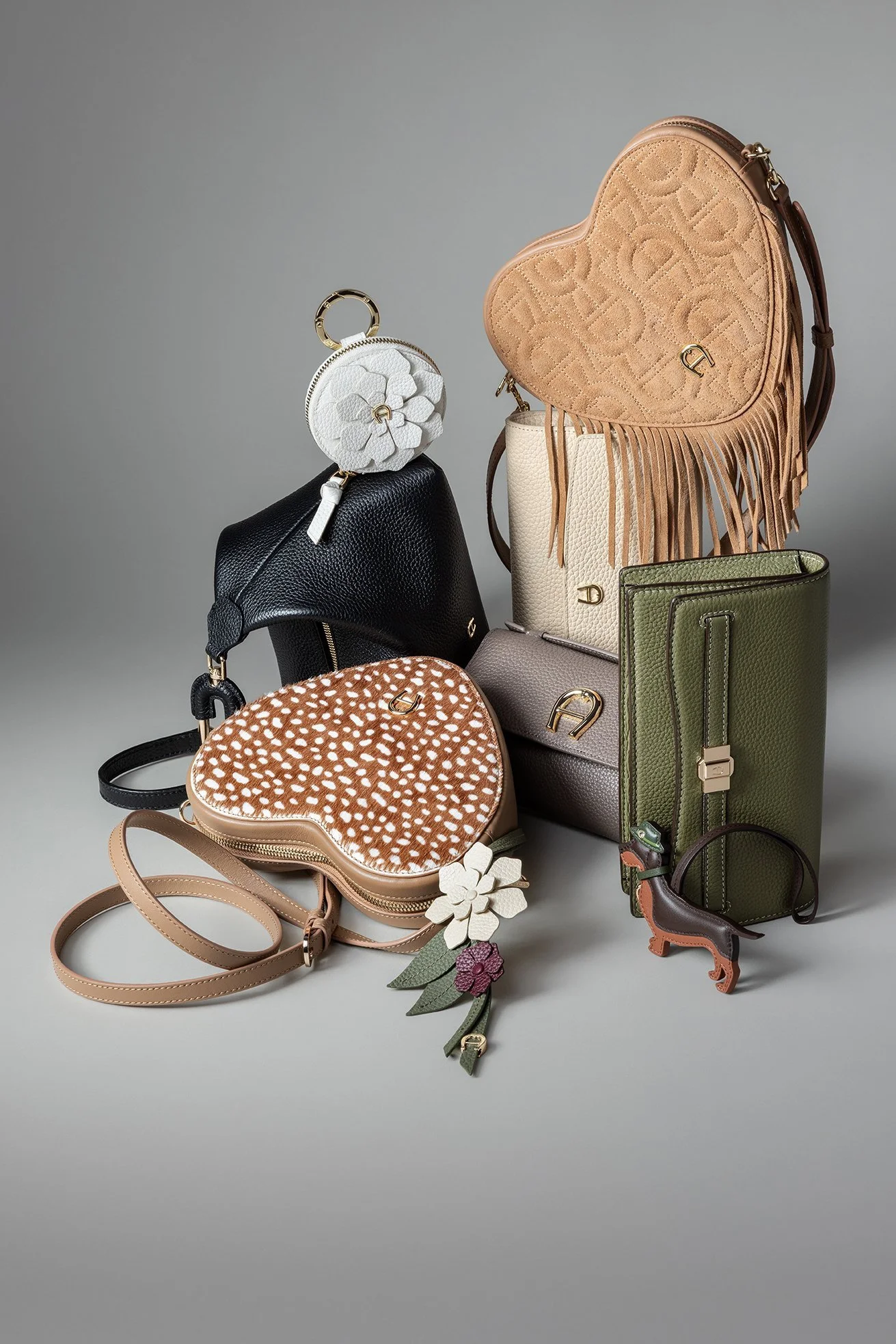 Arrangement von Aigner-Herztaschen, Portemonnaies und Lederblumen in Grau vor neutralem Hintergrund – Retusche Bildergut.