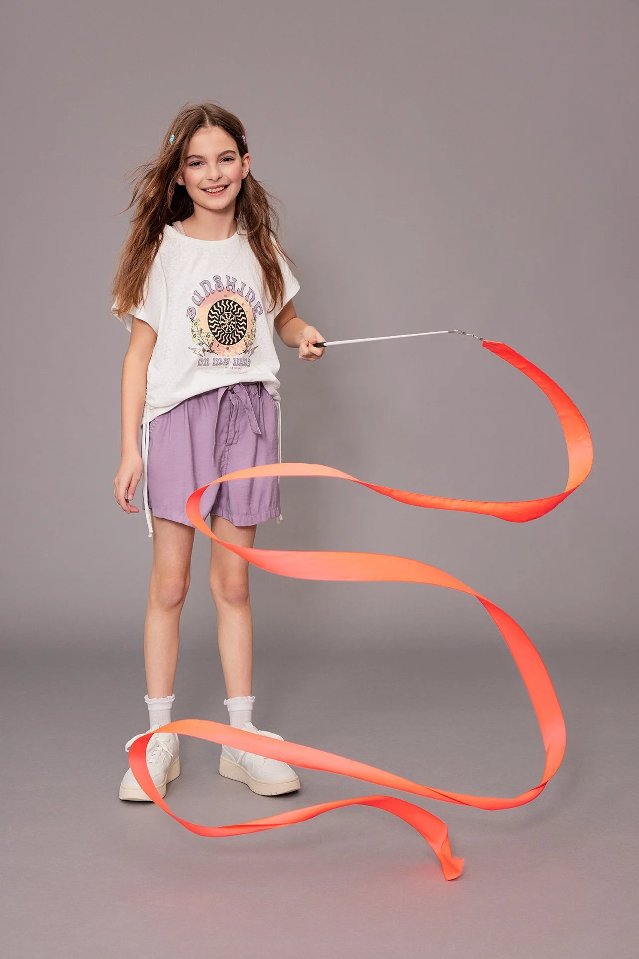 Mädchen schwingt orangefarbenes Gymnastikband im Studio, Kids-Kampagne Frühjahr-Sommer 2023 für Zinser – Retusche Bildergut.