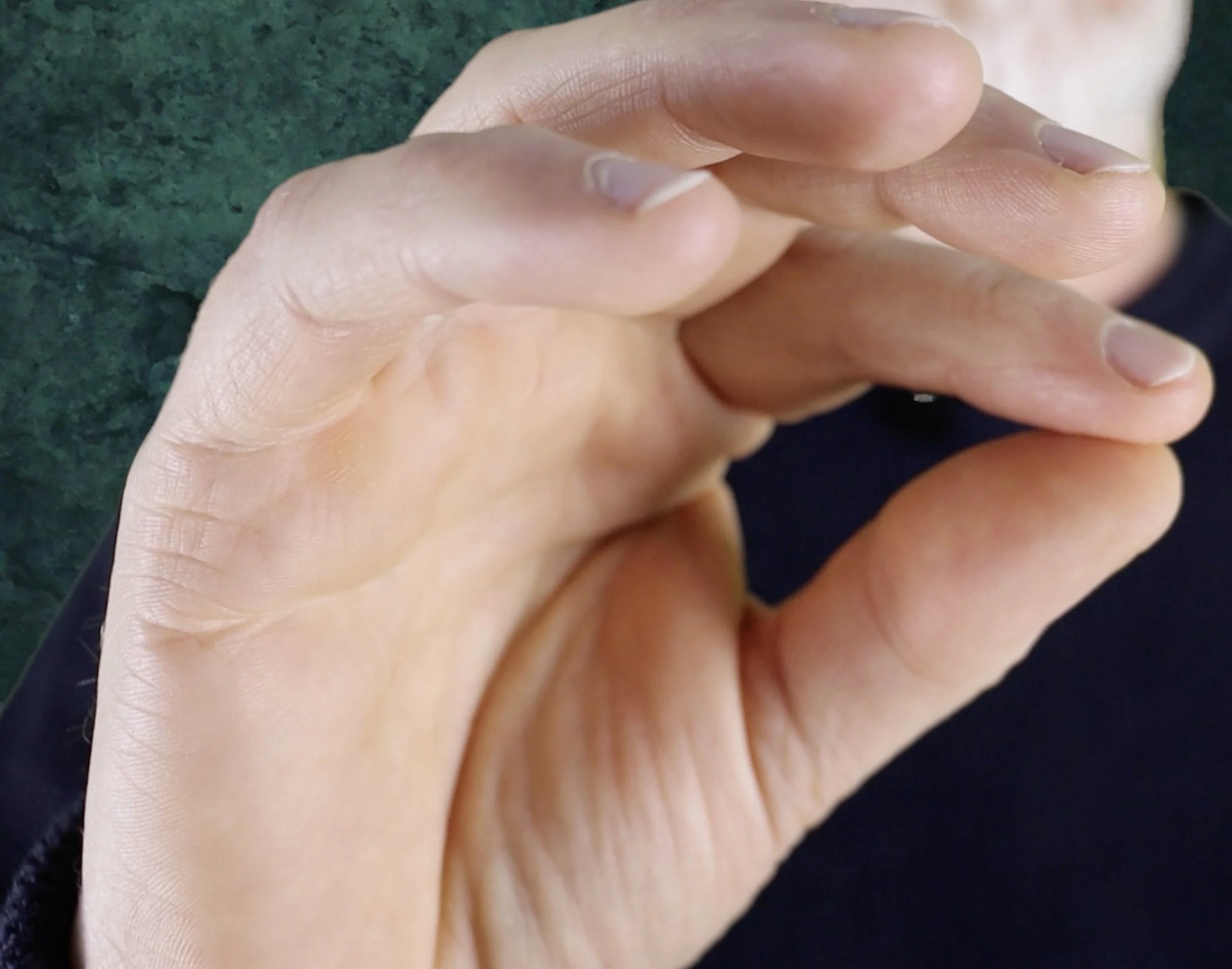 Nahaufnahme von zwei menschlichen Händen, die leicht übereinander liegen und auf einer grünen Oberfläche ruhen. Modul 8. Kinesiologie bei Tinnitus.