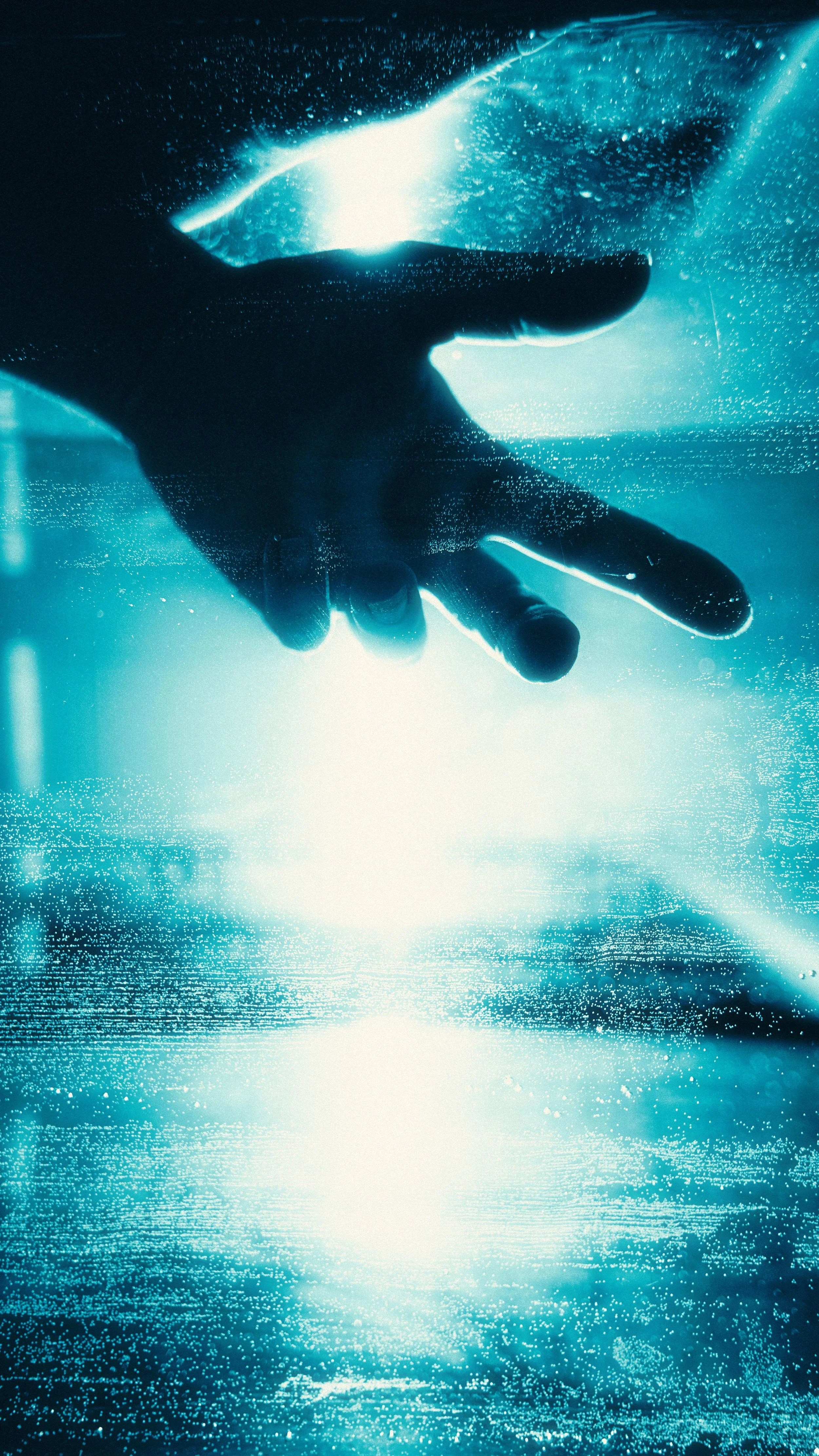 Hand, die durch eine Glasscheibe in Wasser taucht, mit Blasen und Lichtreflexionen. Modul 7 mPET bei Tinnitus.